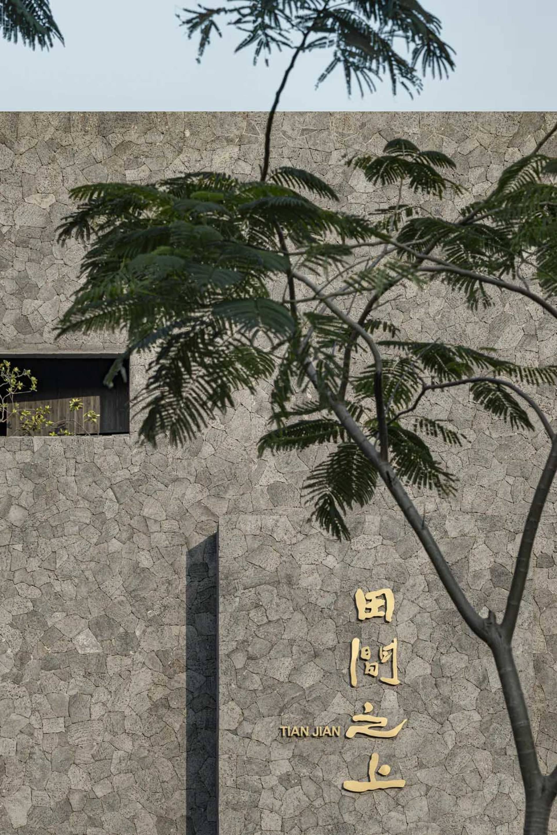 Asian-style building with stone exterior, two trees in front, and a wall with Chinese characters