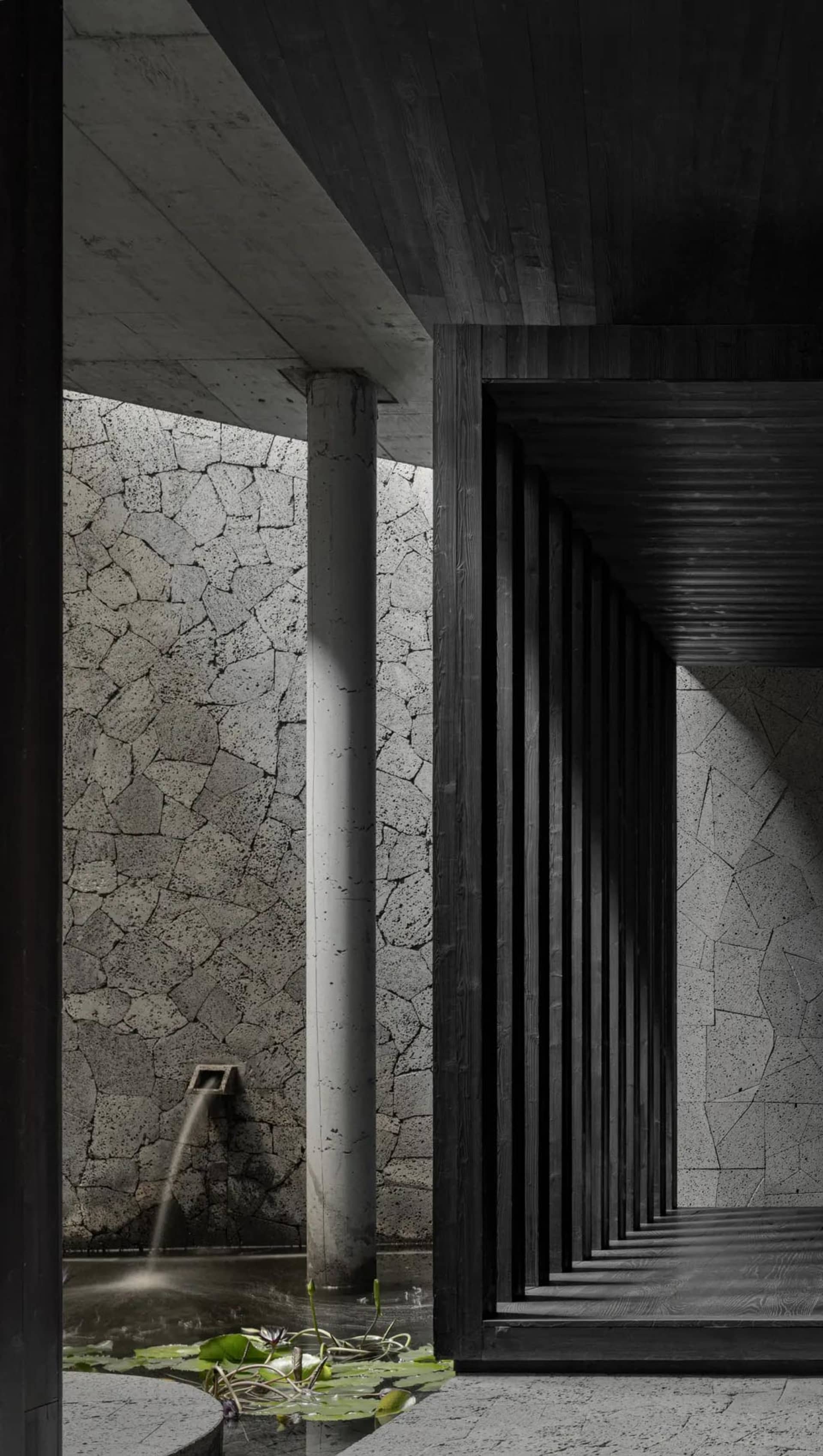 A stone hallway with two pillars on either side of the passage, leading to a doorway in a darker area of the building