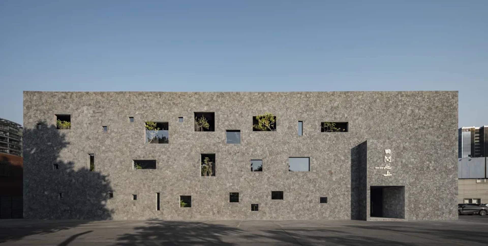 A modern building with a stone exterior, featuring multiple windows in various shapes and sizes, creating a diverse appearance