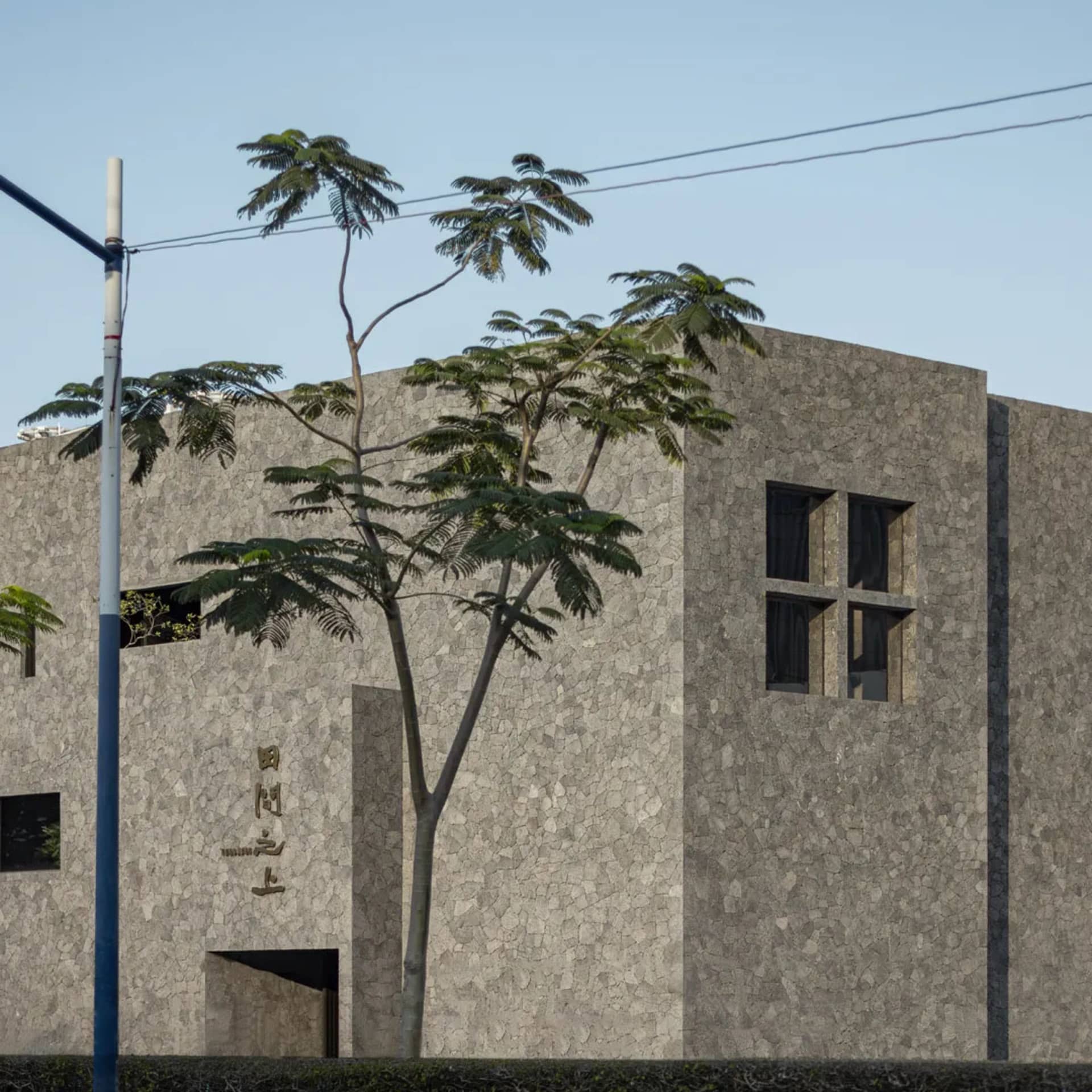 A modern building with a gray stone exterior, featuring a tree in front and two crosses on the side, set against a clear sky