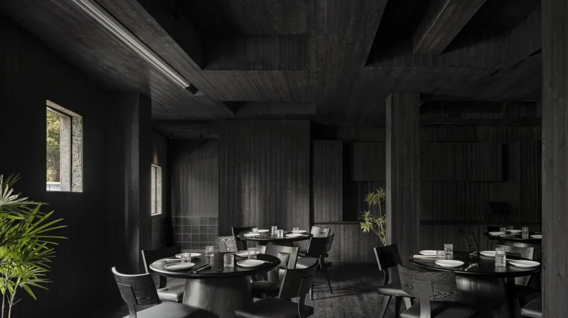 A dark and moody restaurant with a black and white theme, featuring a dining area with tables and chairs, and cups on some tables