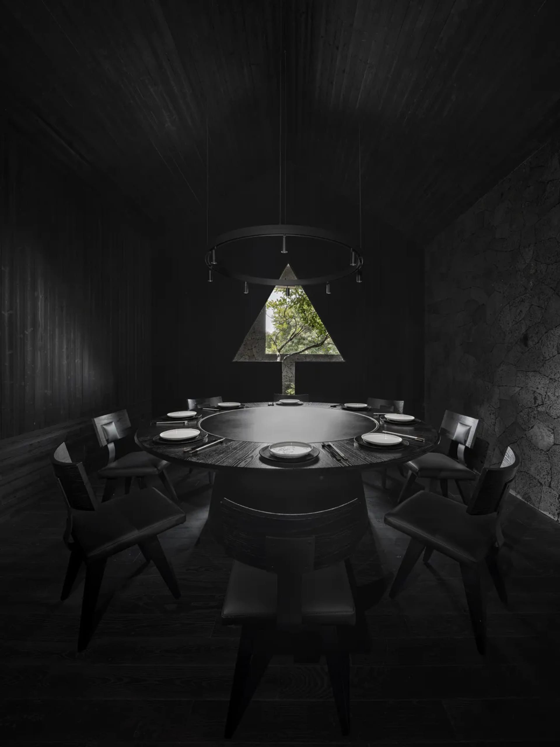 A darkened dining area with a round table and various modern chairs, creating a mysterious atmosphere