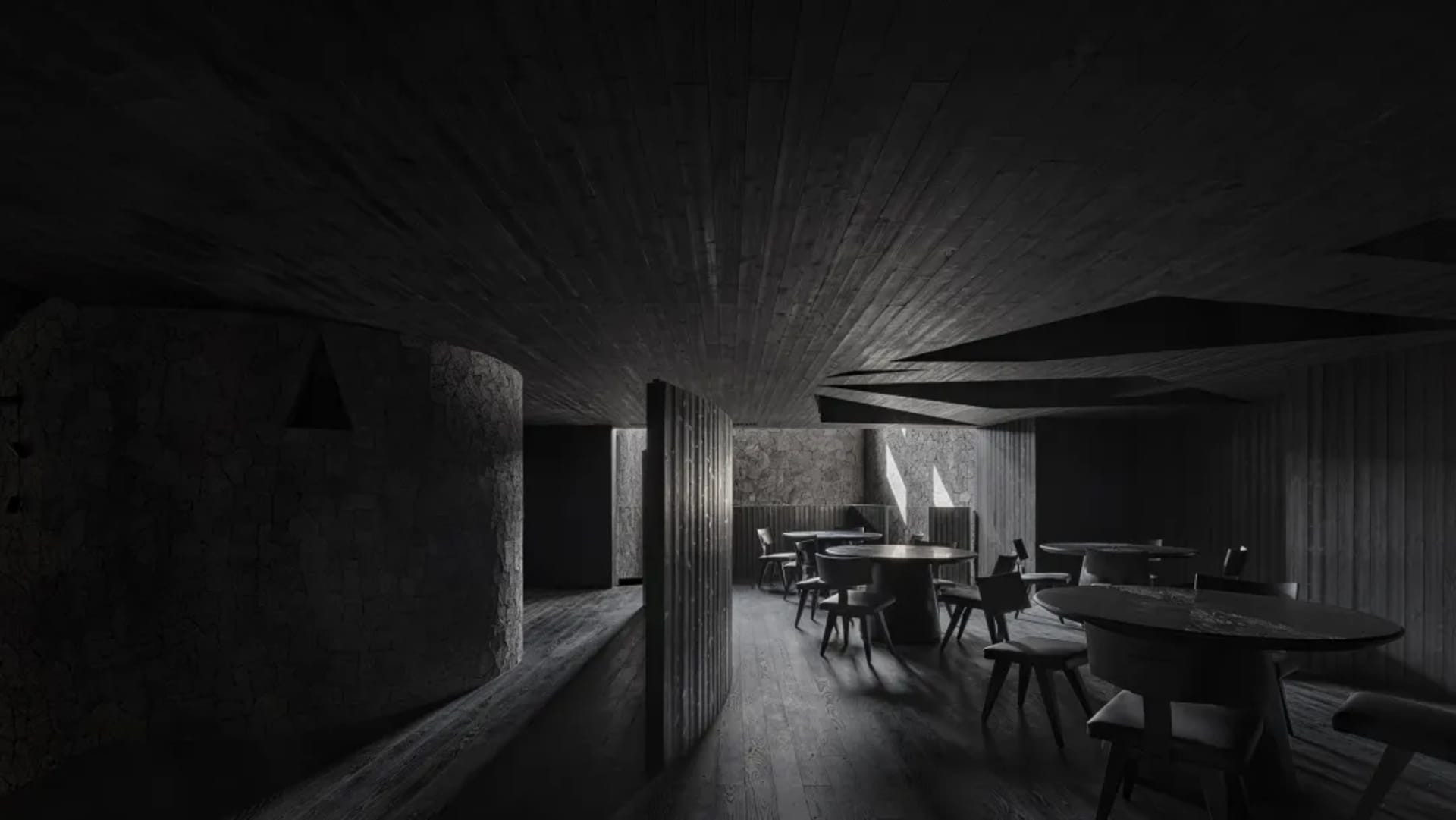 Dark and moody restaurant interior with multiple tables and chairs, wood and stone elements, and minimal natural light