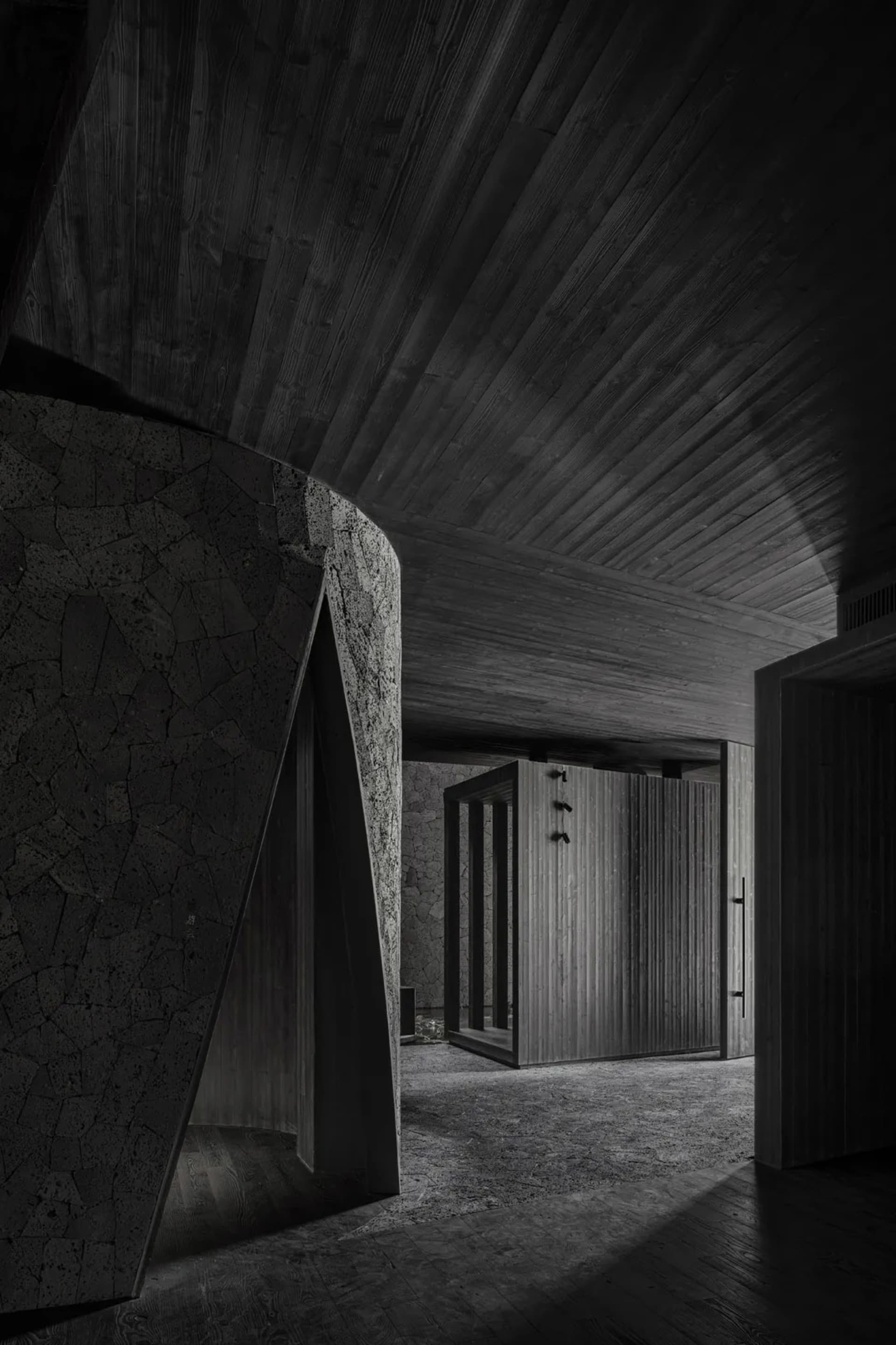 A dimly lit hallway with stone walls, featuring two darkened rooms with doors on either side