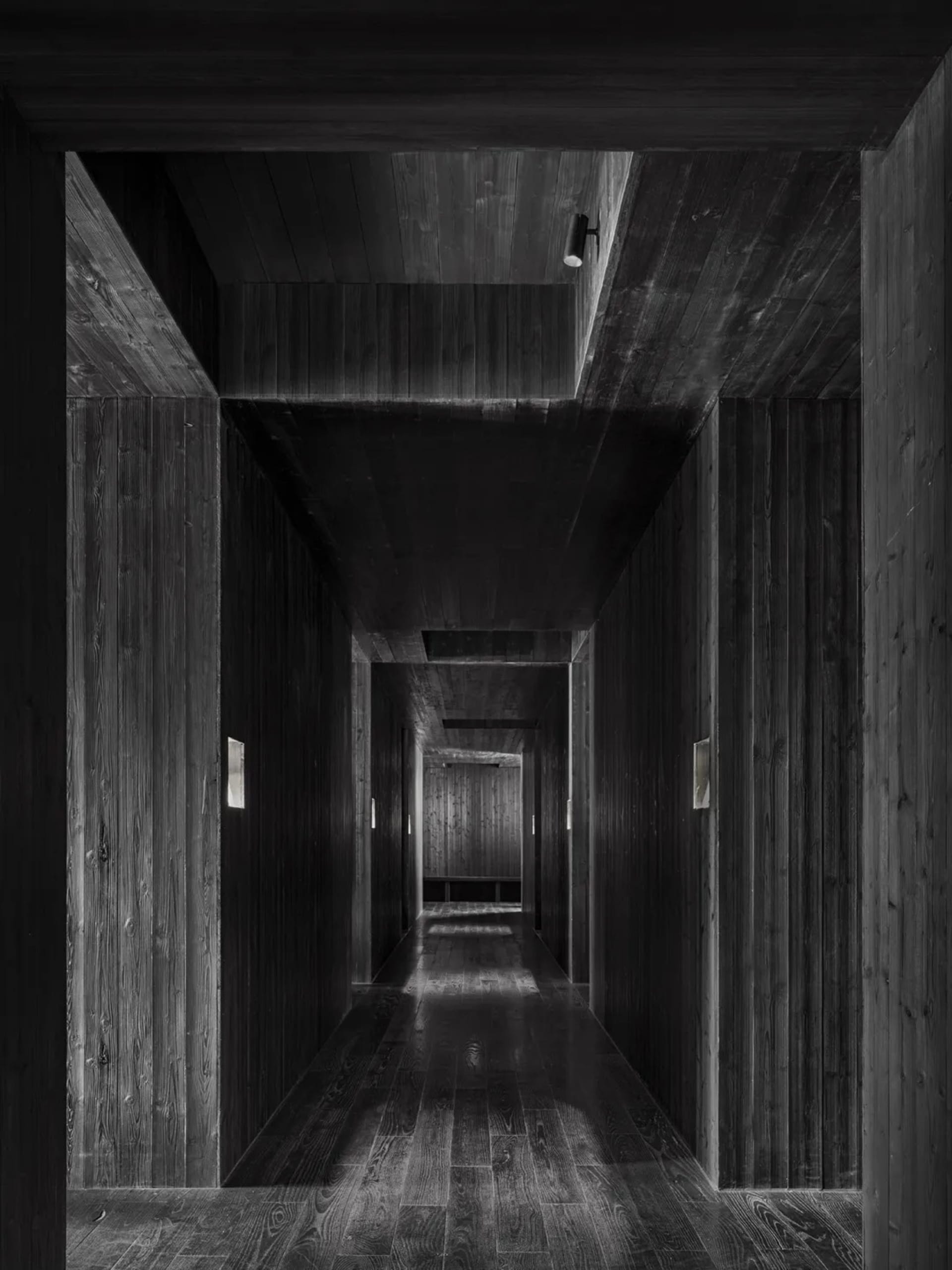 A dark and empty hallway with a wooden floor, devoid of people or objects, creating a sense of mystery
