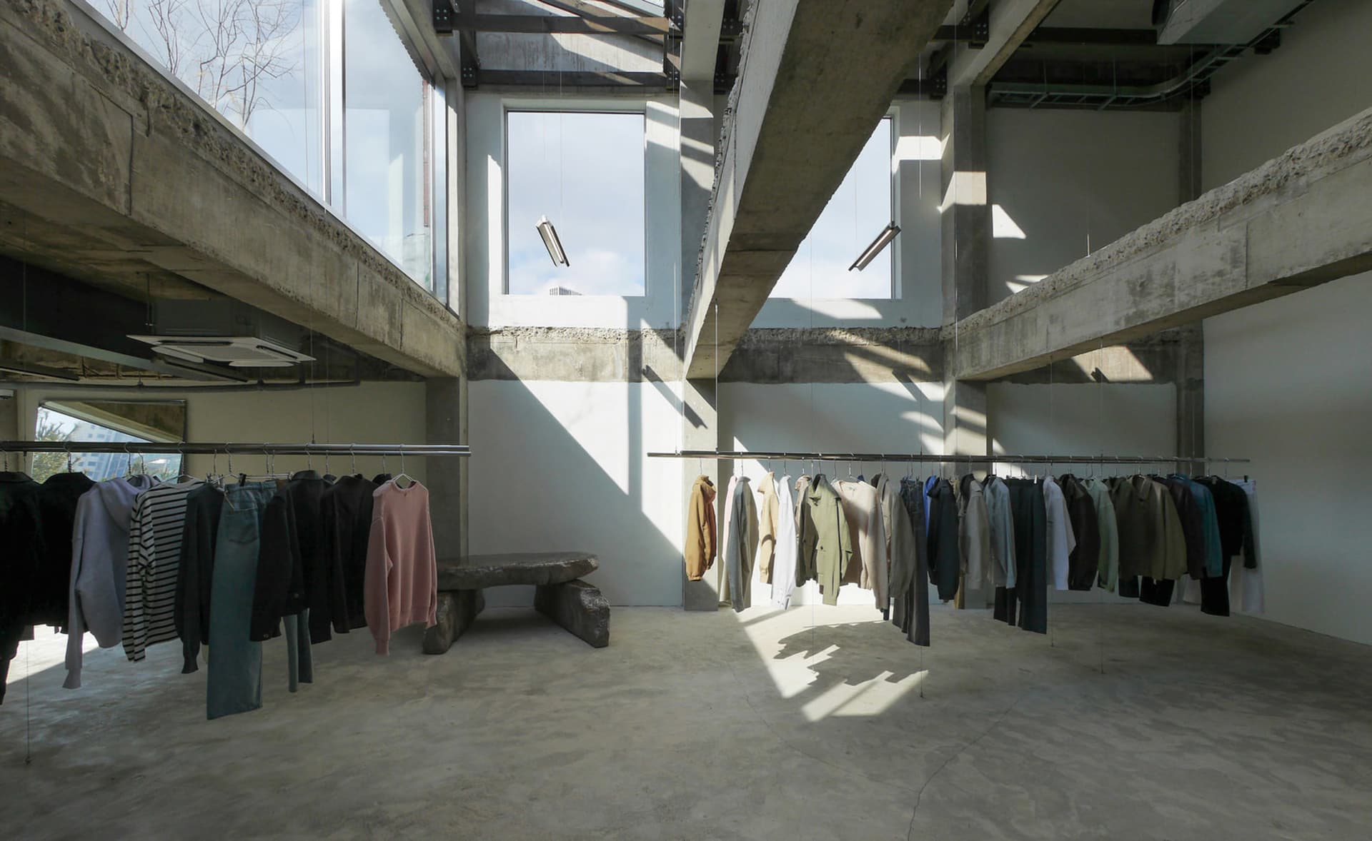 Open clothing store with multiple racks and benches, displaying a variety of garments and accessories