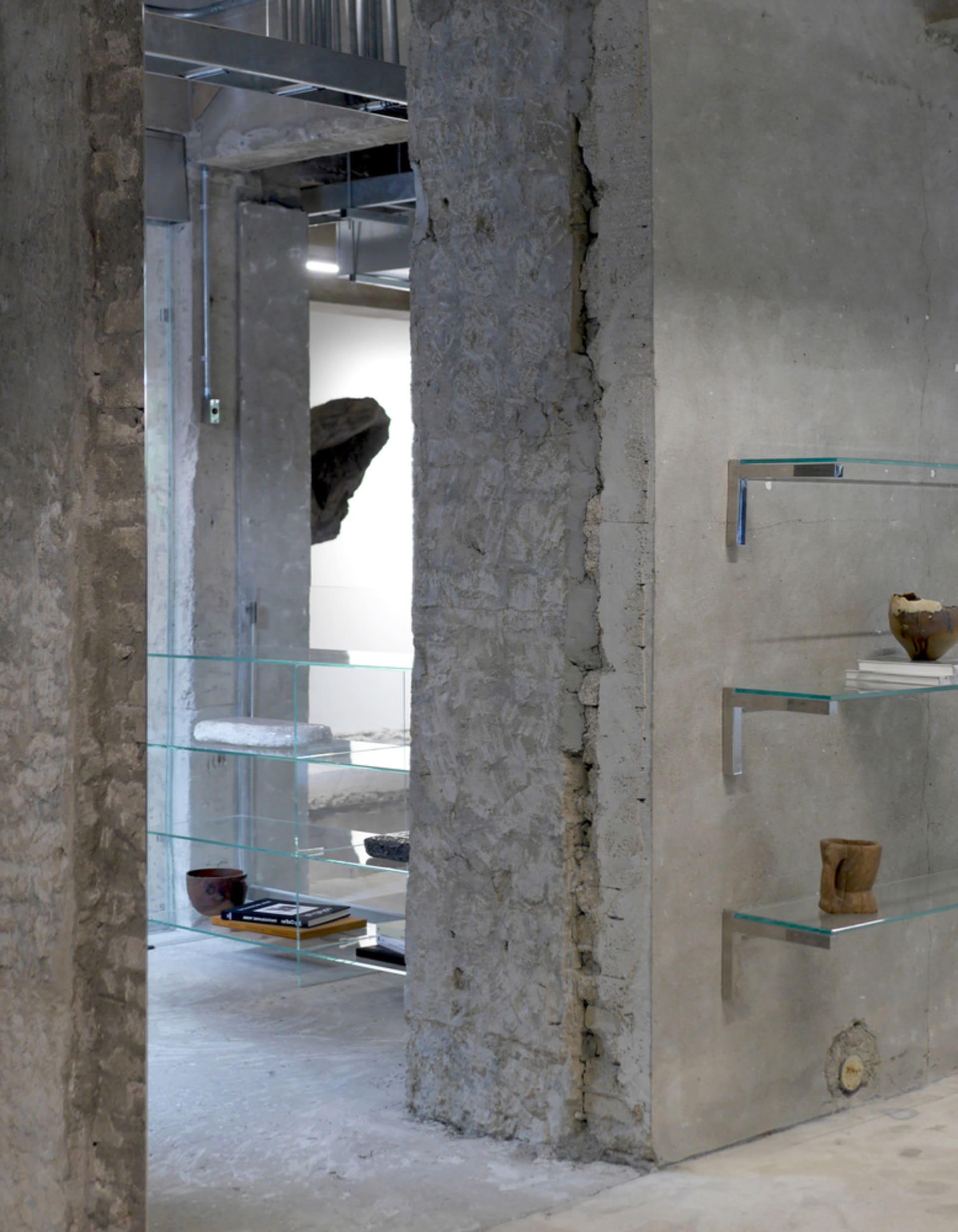 A well-lit art gallery with a display case filled with vases, bowls, and books, set against industrial concrete walls and illuminated by overhead lights