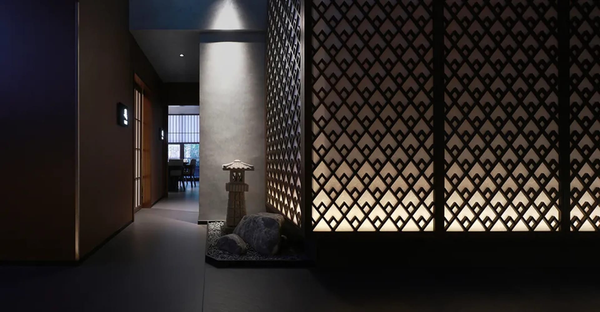 A serene hallway with a rock garden in the center, stone floor, and lights at varying heights, surrounded by Asian-style interior design elements