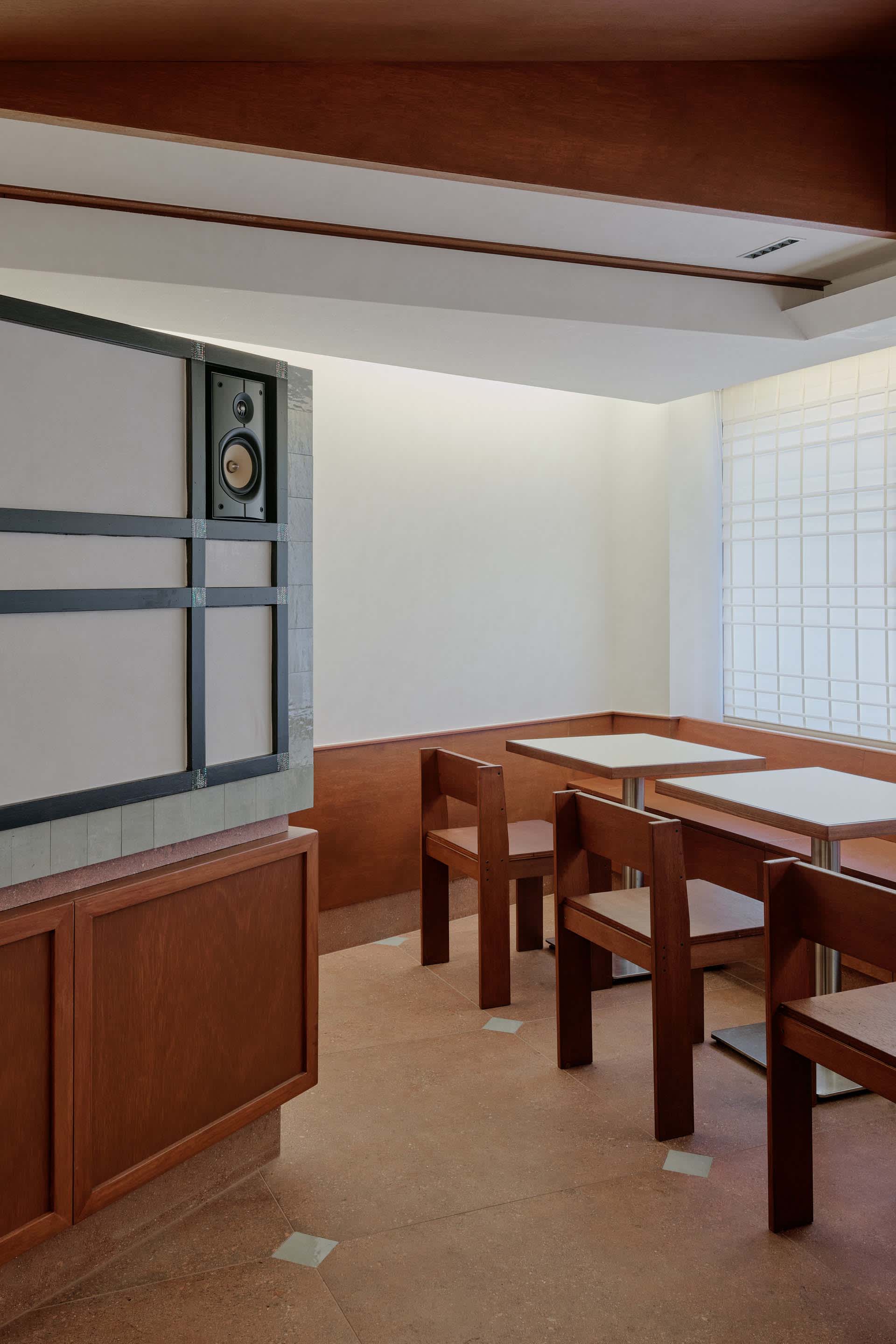 Empty restaurant with wooden tables and chairs, brown walls, and well-designed lighting