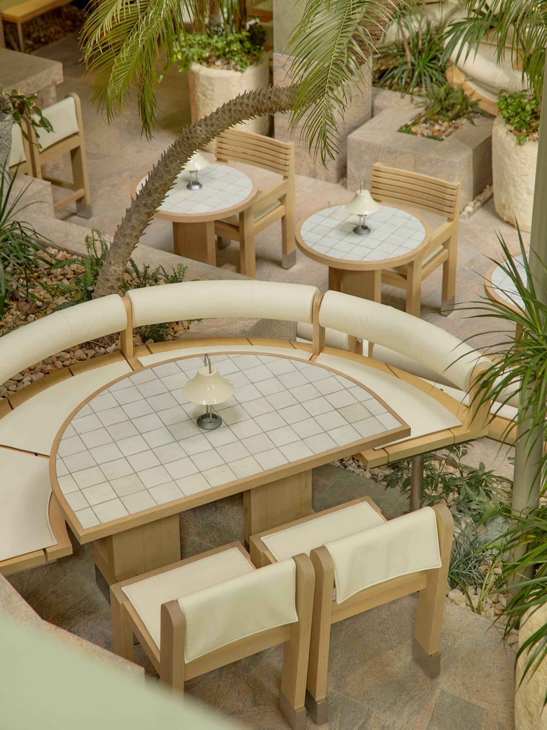 A warm and inviting outdoor dining area with wooden tables and chairs, surrounded by potted plants and a comfortable seating arrangement