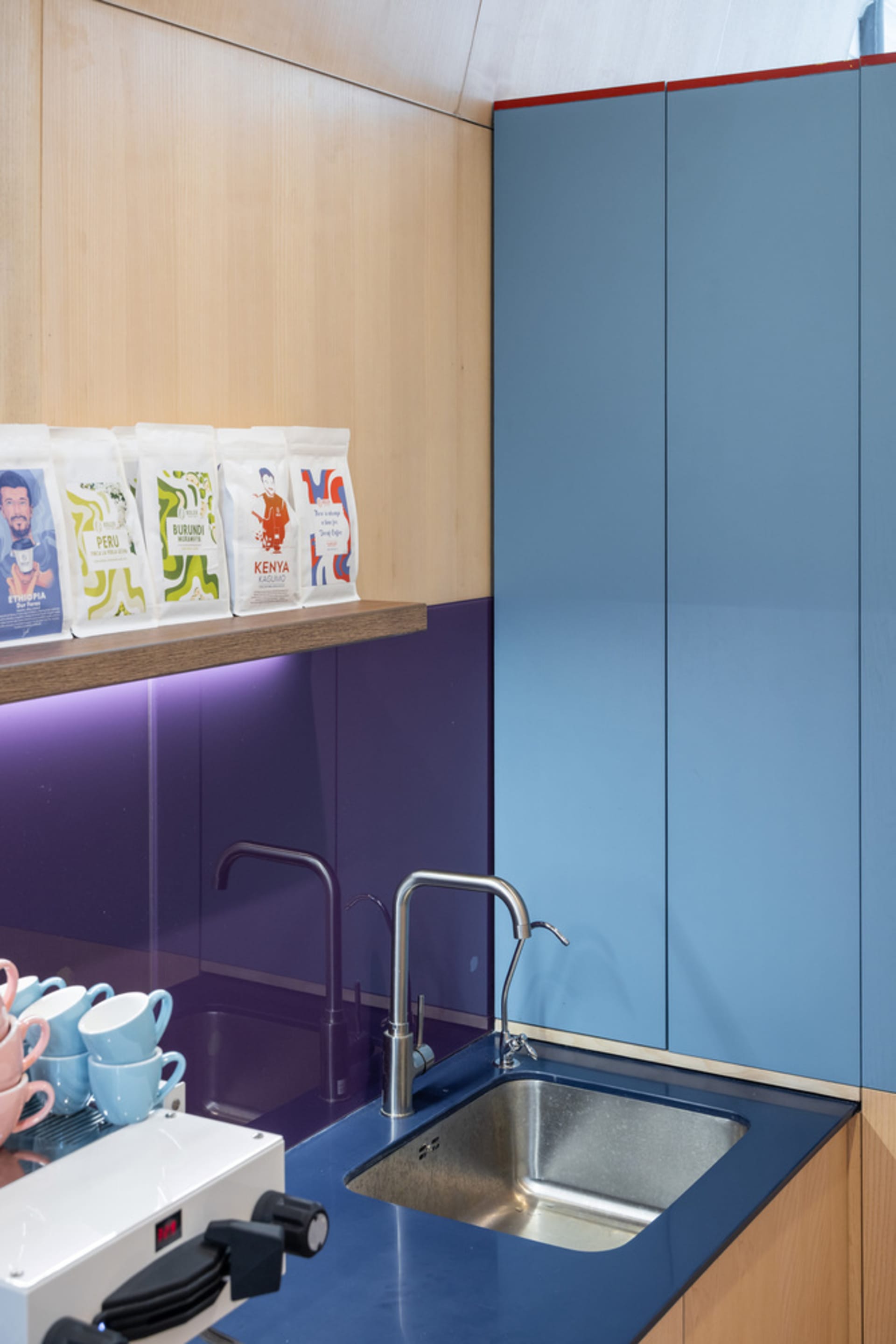 A modern kitchen with purple walls, a sink, and a countertop with cups and coffee beans, giving a clean and organized atmosphere