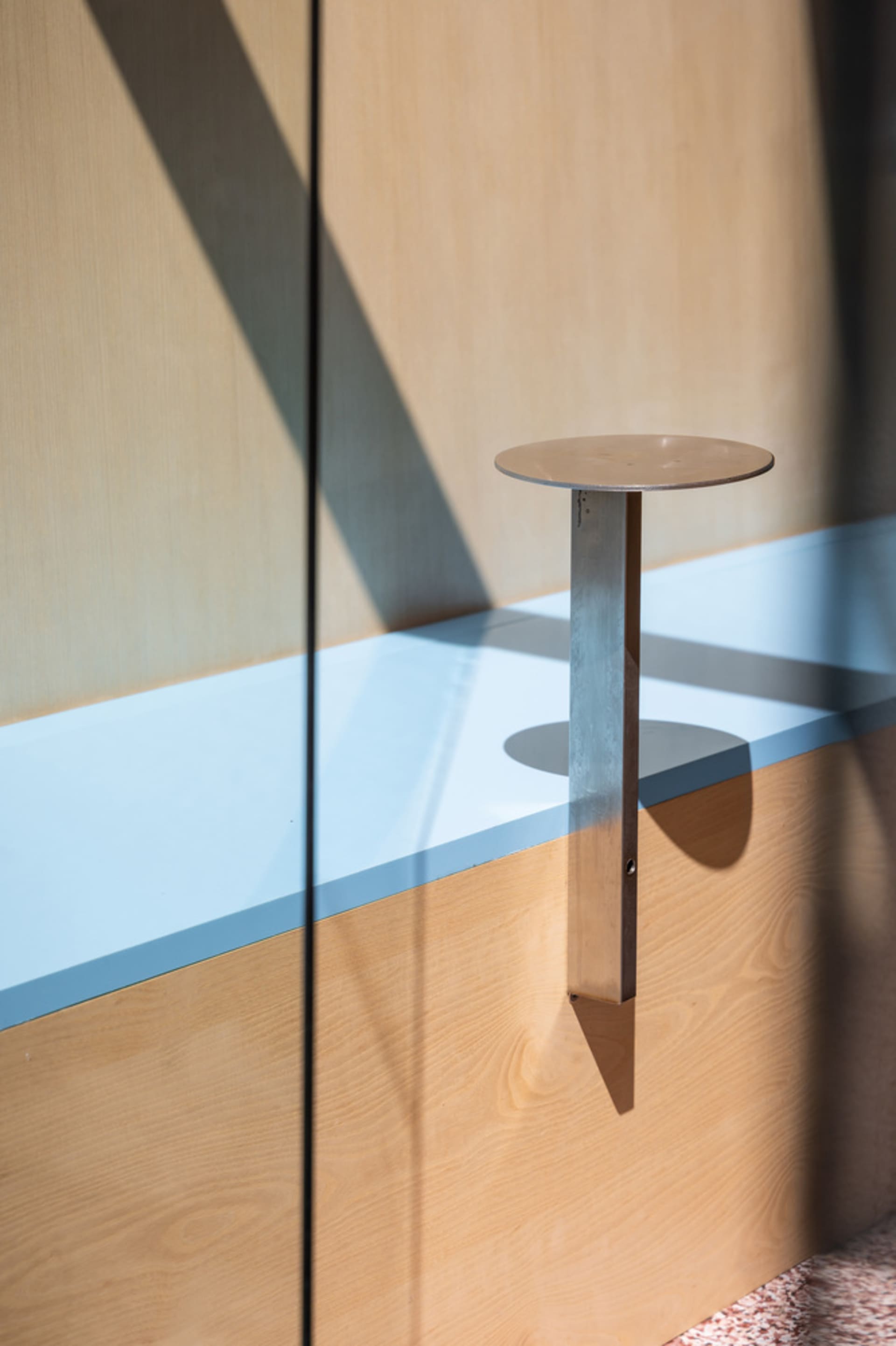 A modern dining space with a wooden table and metal base in front of a glass wall, allowing natural light to create a bright atmosphere
