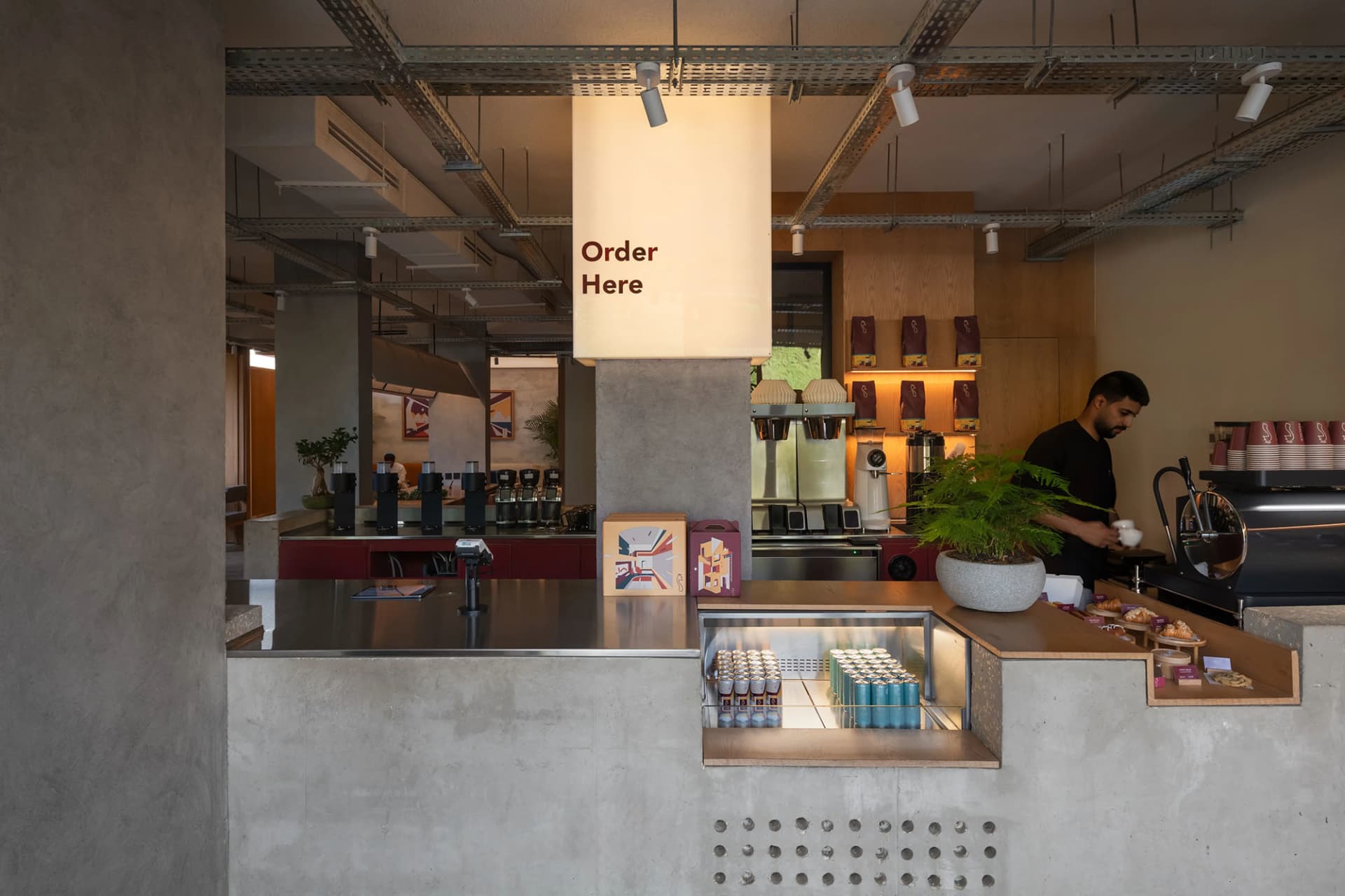 A casual restaurant counter with a cash register, cups, bottles, and potted plants, creating a welcoming atmosphere for customers
