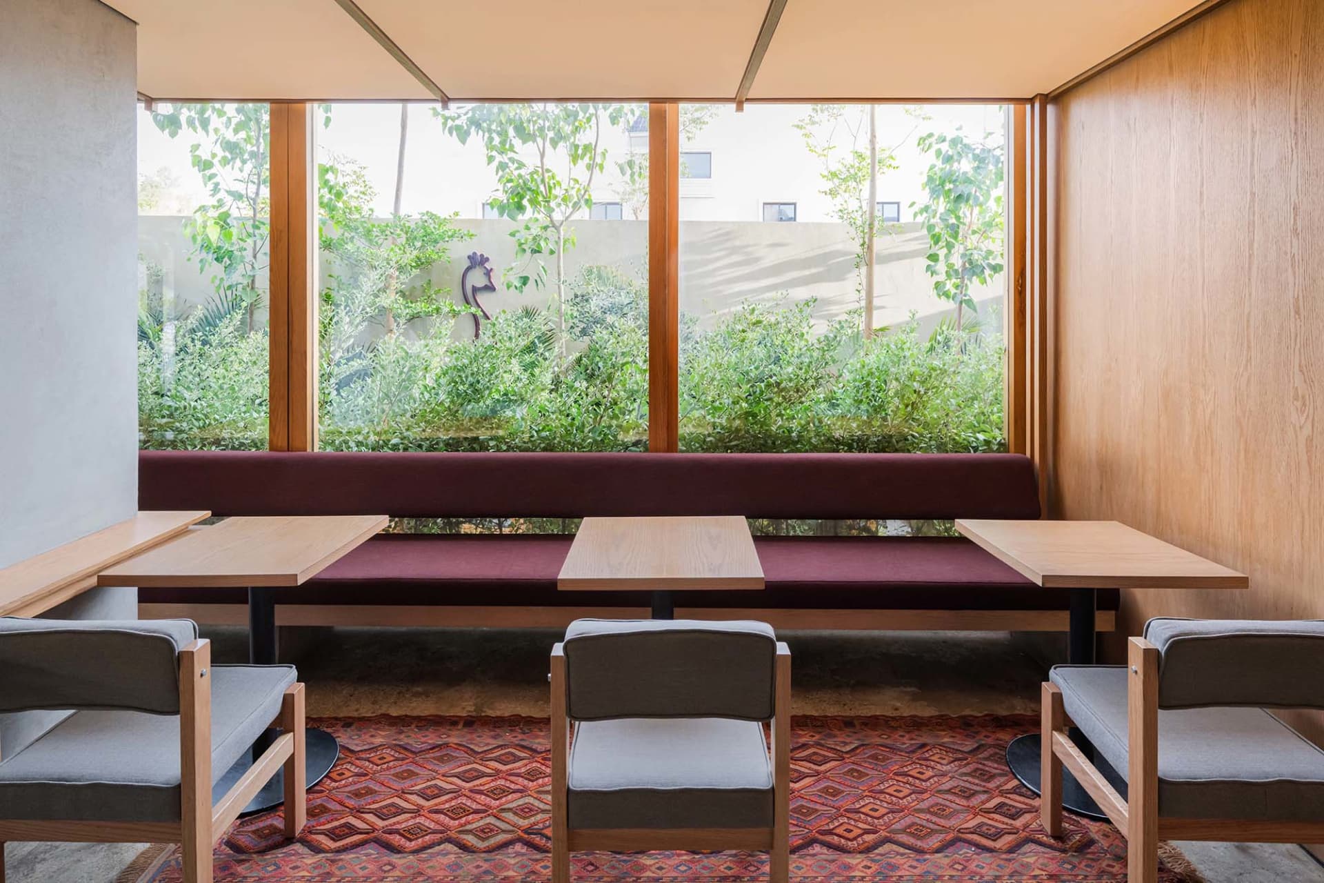 A well-lit dining space with a long bench between two tables, surrounded by chairs and natural light from windows