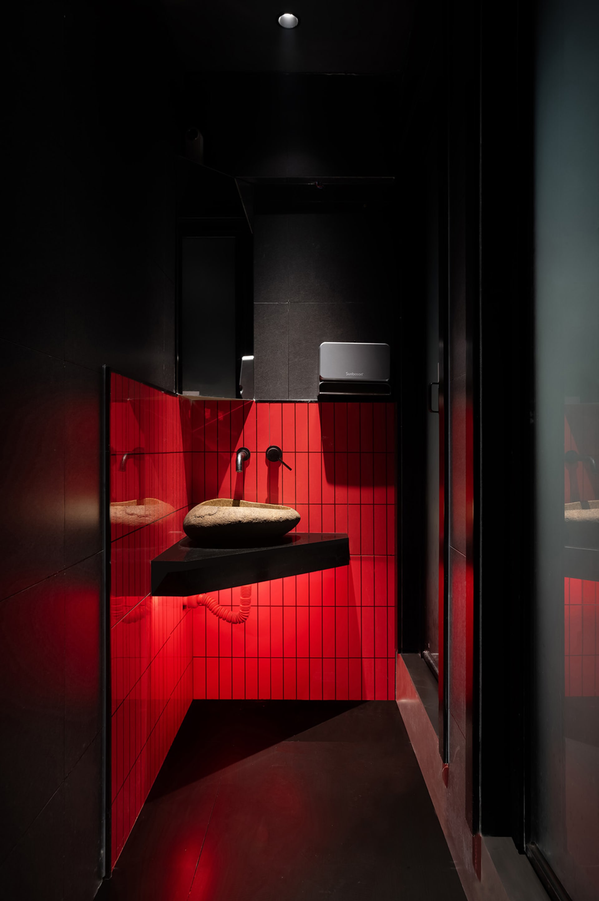 Bathroom with red tile walls and floors, featuring two sinks and mirrors above, giving a modern and sleek appearance