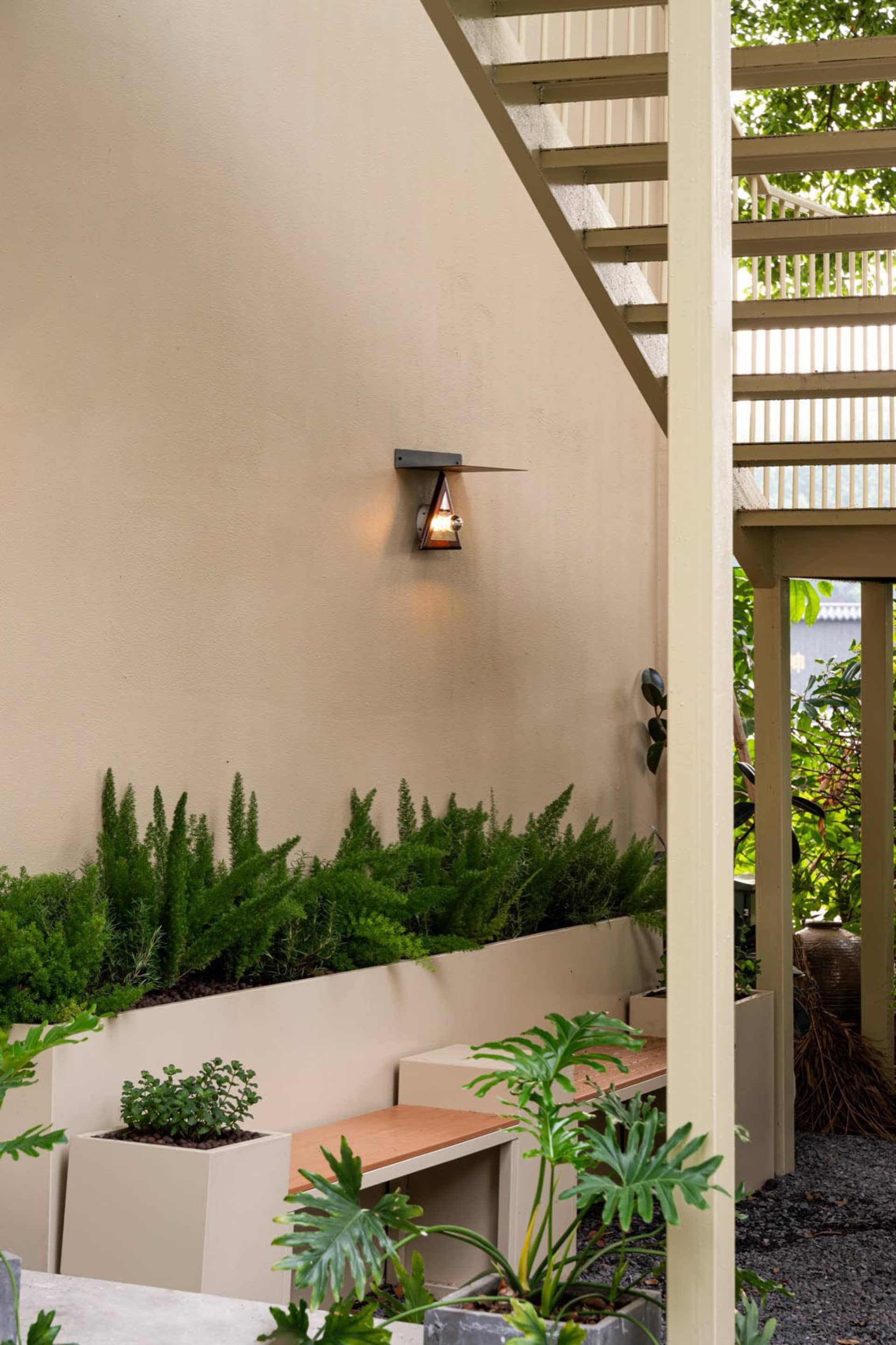 A wooden deck with a bench seating arrangement surrounded by potted plants and a bird, set in a relaxing outdoor space with a focus on greenery and natural elements