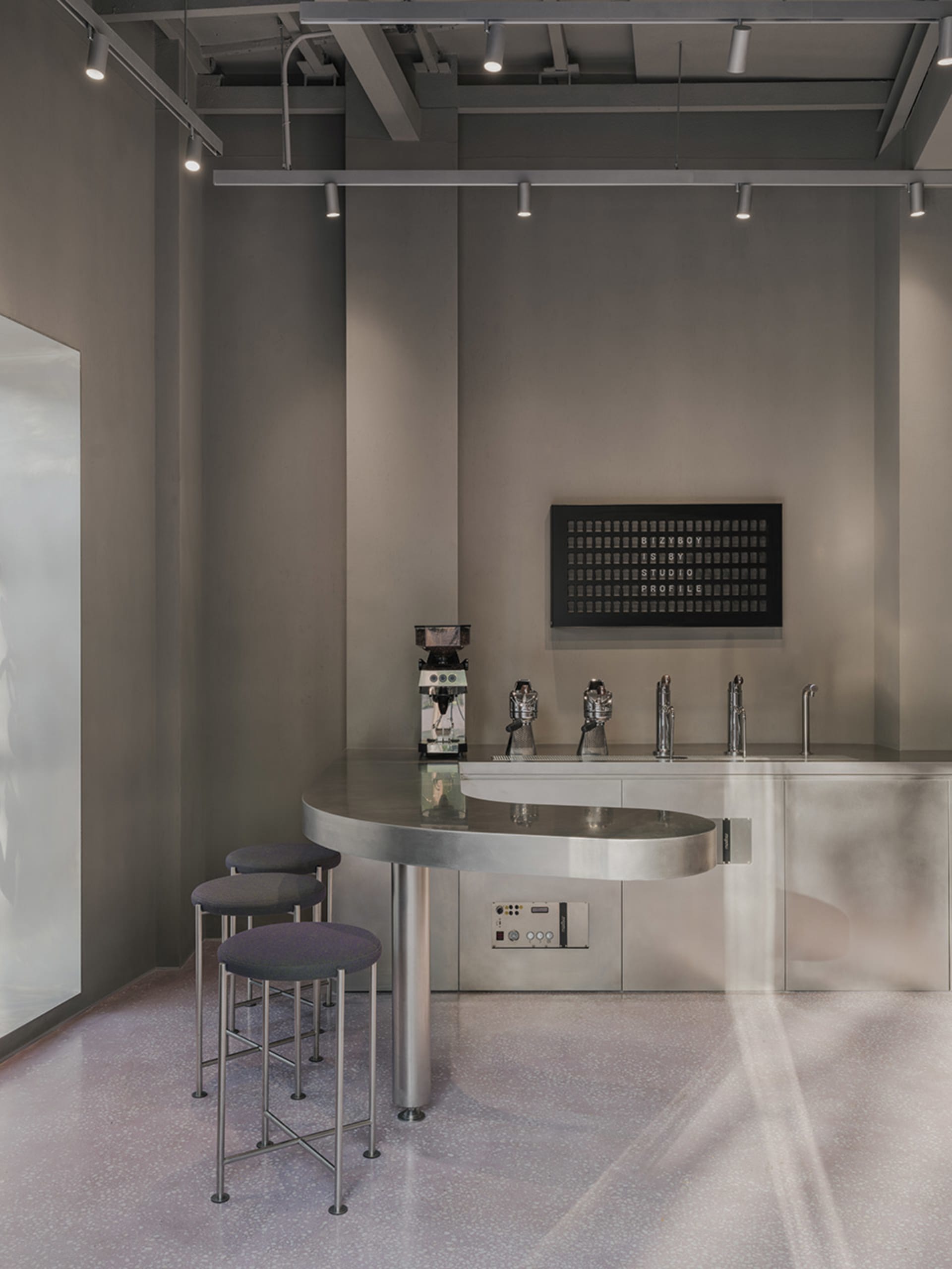 Industrial-style bar with a large metal countertop, beer taps, and stools, set in a modern and functional space