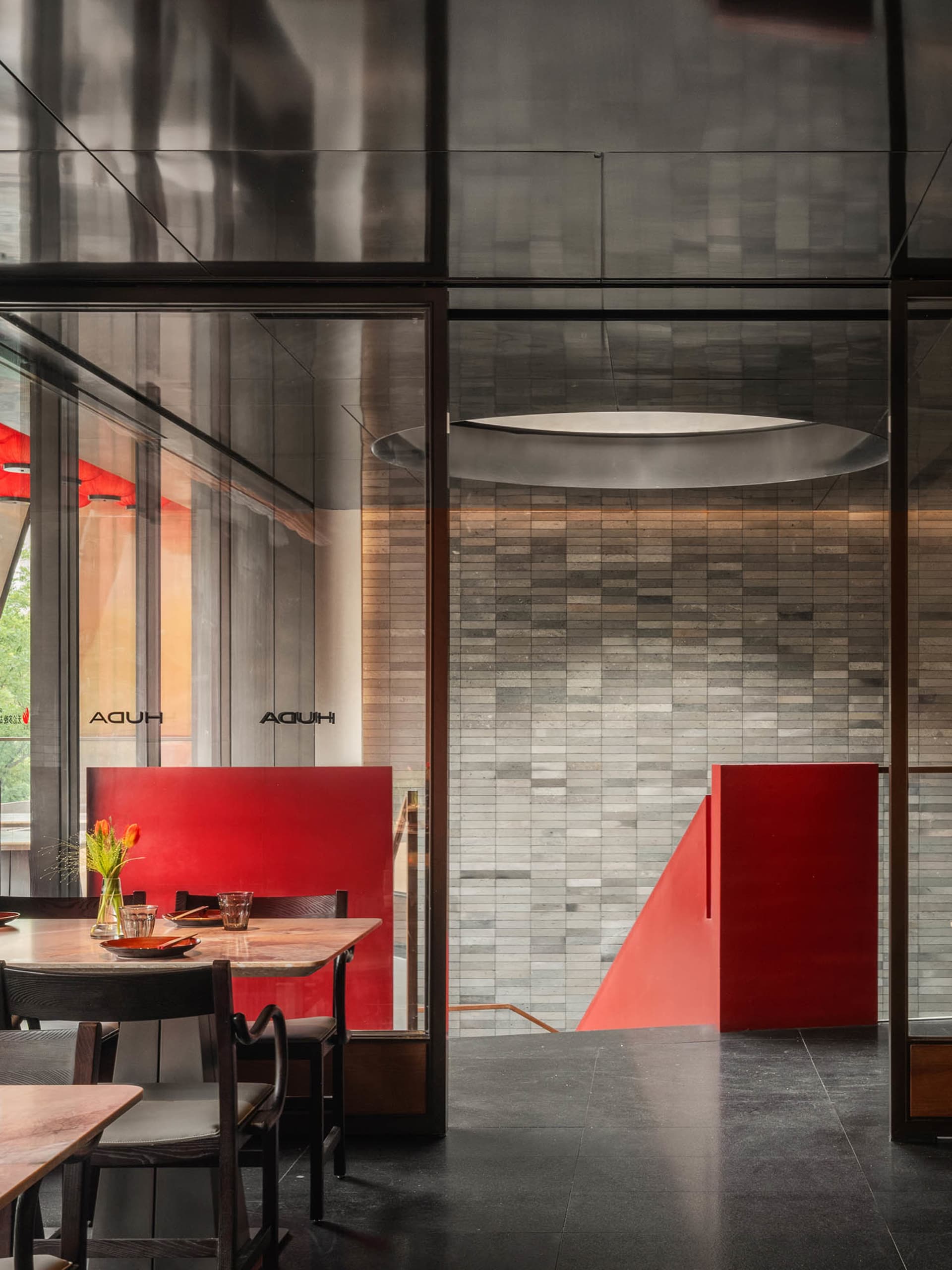 A restaurant interior with red walls, a large window, and two dining tables with chairs, decorative elements like potted plants, vases, and bowls, and a warm ambiance