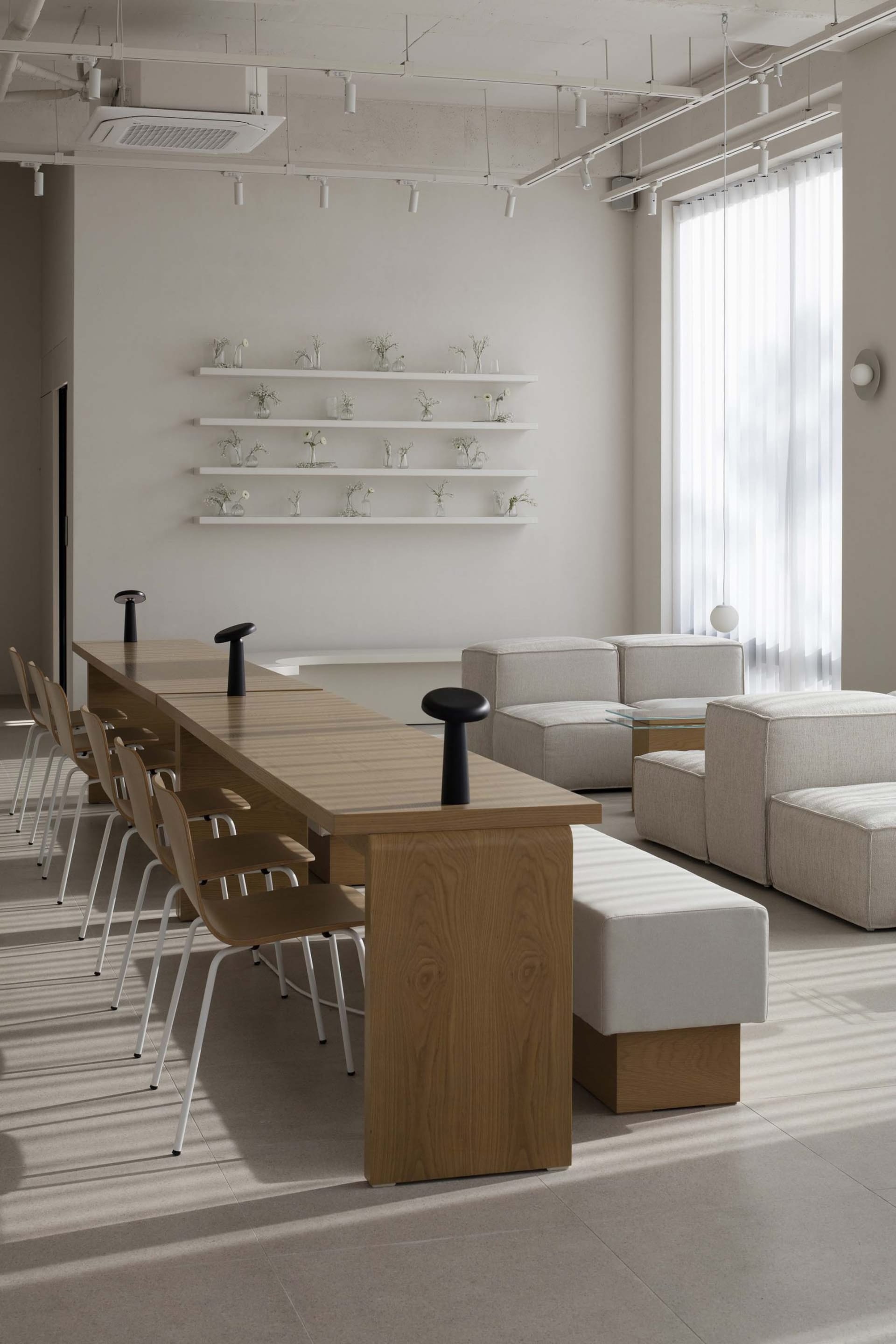 A modern living room with a wooden dining table surrounded by eight chairs, set against a backdrop of white walls and a clean, minimalist design
