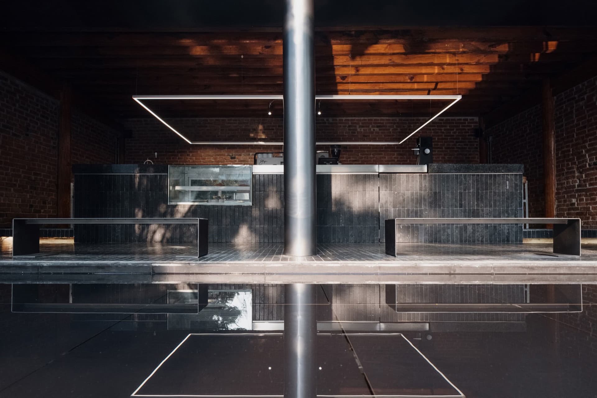 Modern bar interior with a black countertop, brick wall, and metal pole, featuring benches and a sophisticated atmosphere