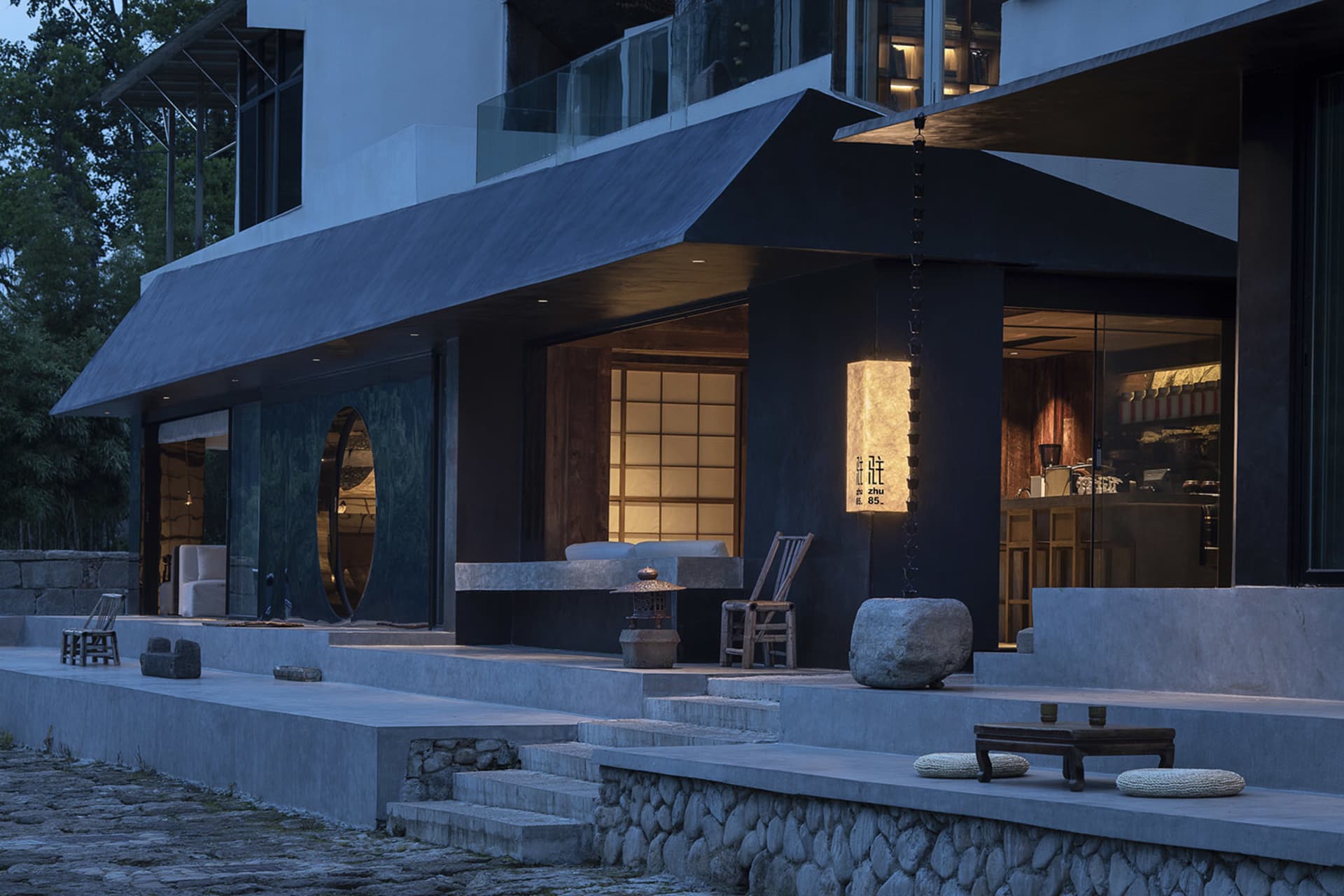 A modern house at night with a stone facade, featuring a kitchen area, dining table, and two benches in an elegant and sophisticated atmosphere