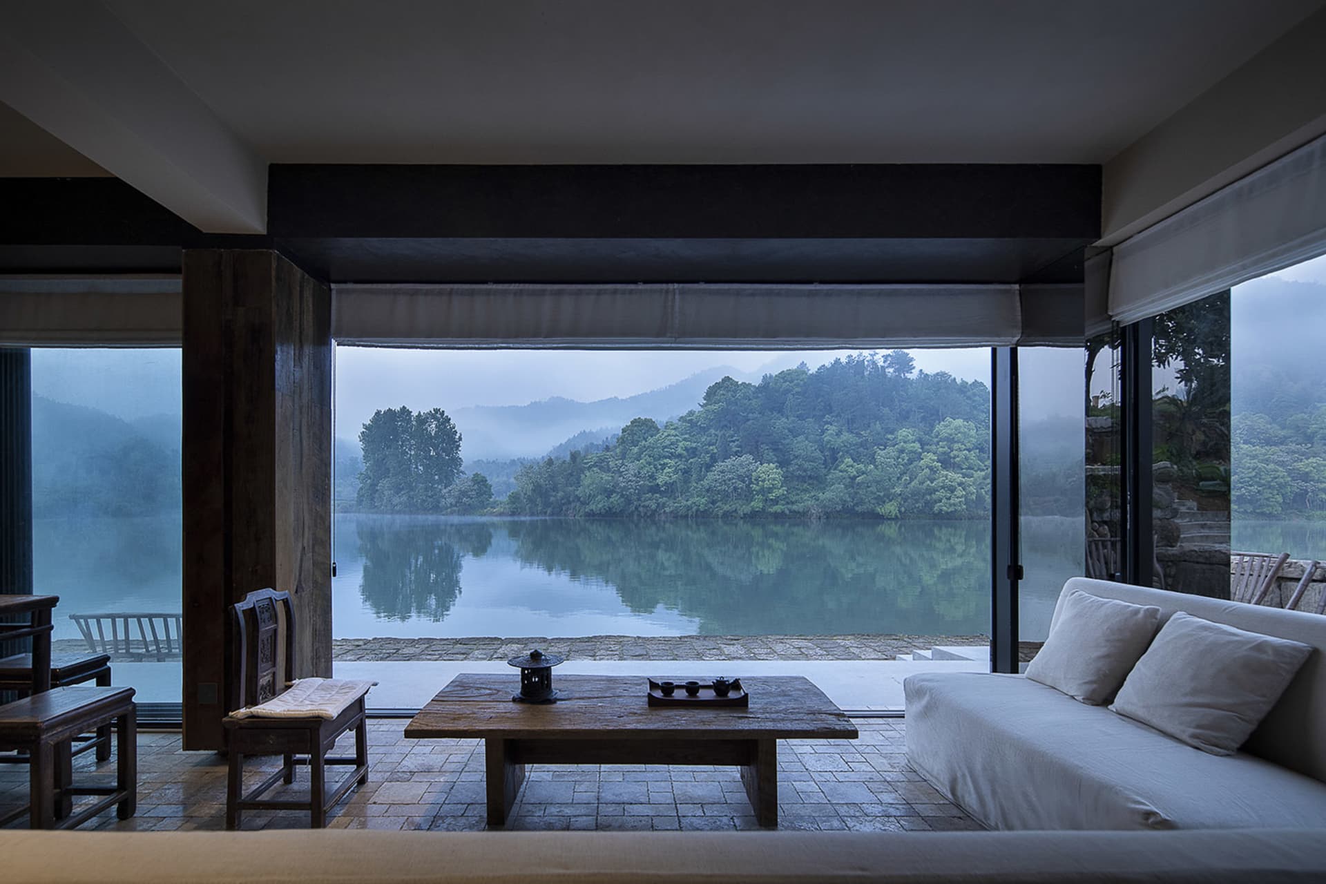 Cozy indoor living area with a large window overlooking a lake, featuring two couches, a dining table, and chairs, with a focus on relaxation and enjoying the view outside