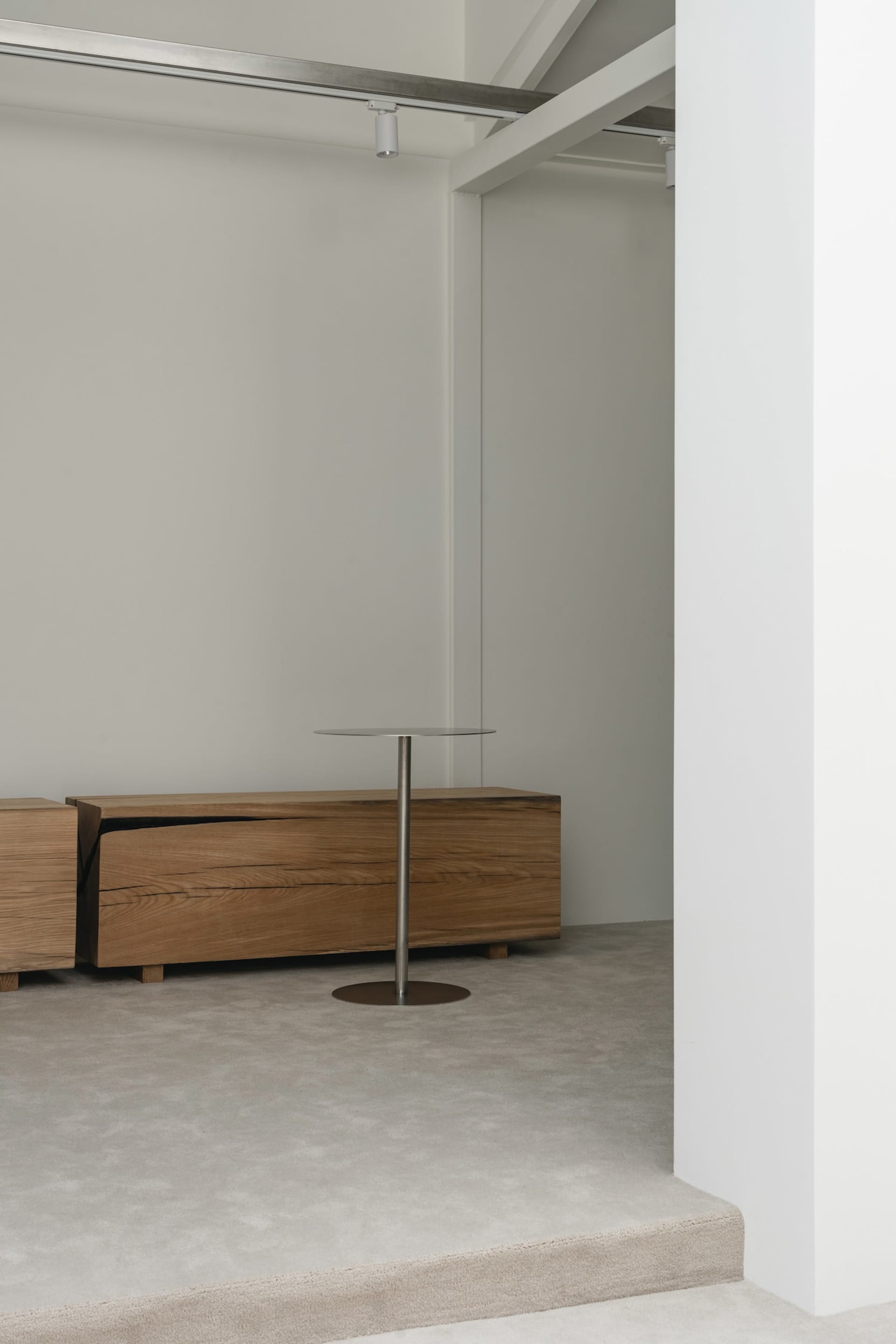 Modern living room with wooden floors and white walls, featuring two wooden dressers and a metal table, with a clean and minimalist design