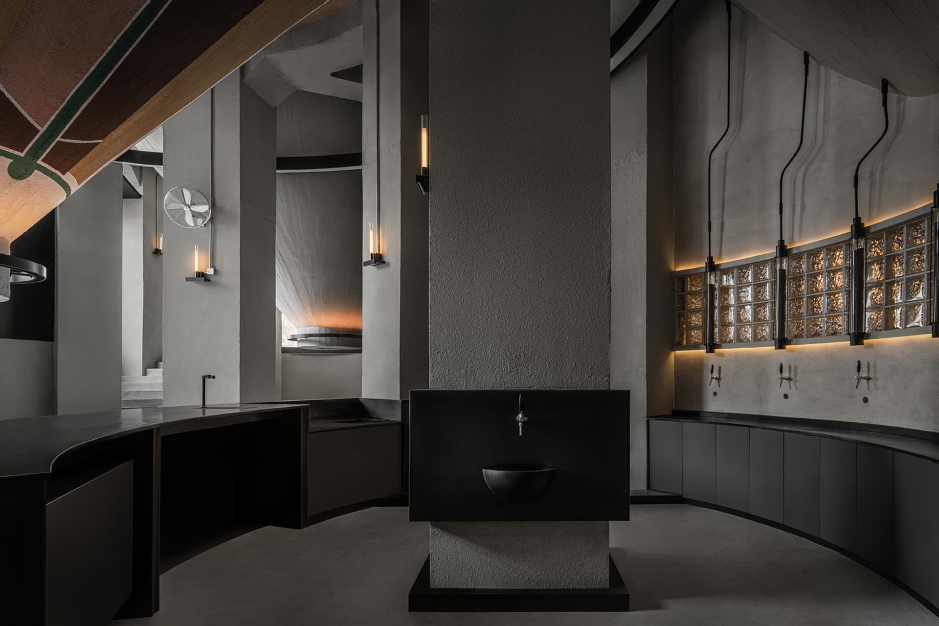 Empty modern bathroom with a black sink and a large stone wall, illuminated by a few lights