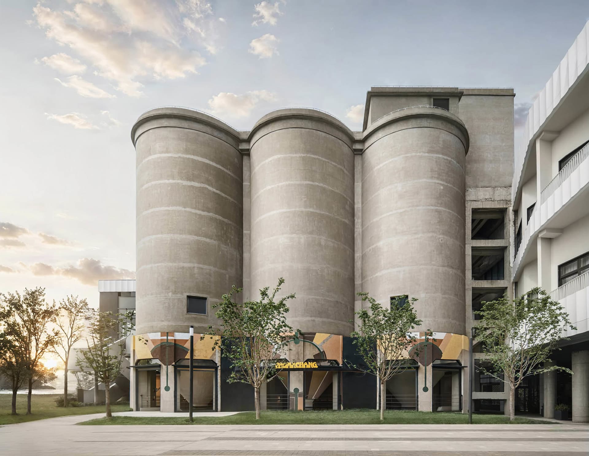 A large building with a modern industrial feel, featuring a circular structure, concrete appearance, and ample natural light from multiple windows