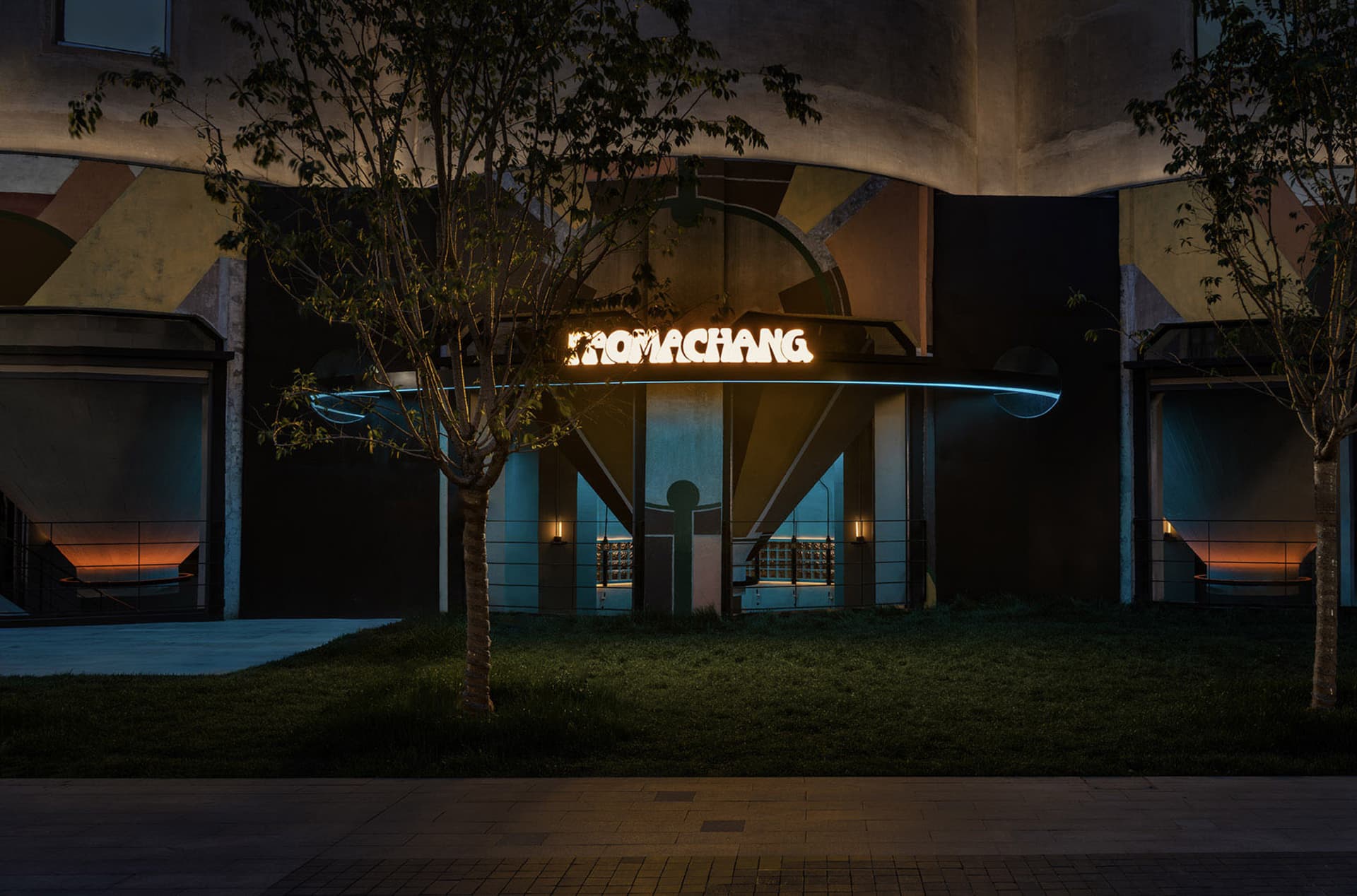 現代建築夜景，擁有醒目圓形結構，前景有兩張椅子