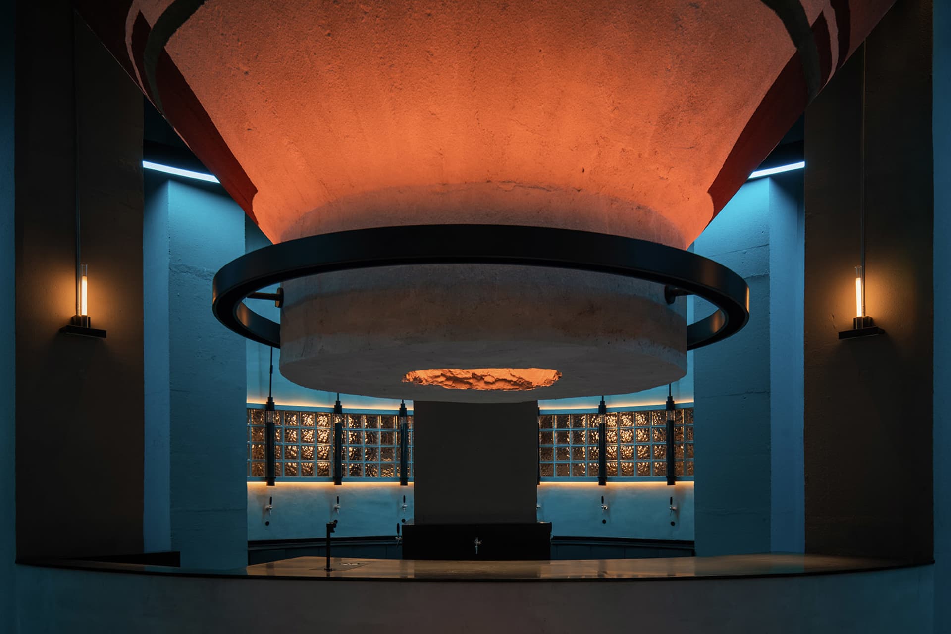 A large stone wall with a circular opening in the center, set against a minimalist industrial backdrop with a sense of depth and dimension