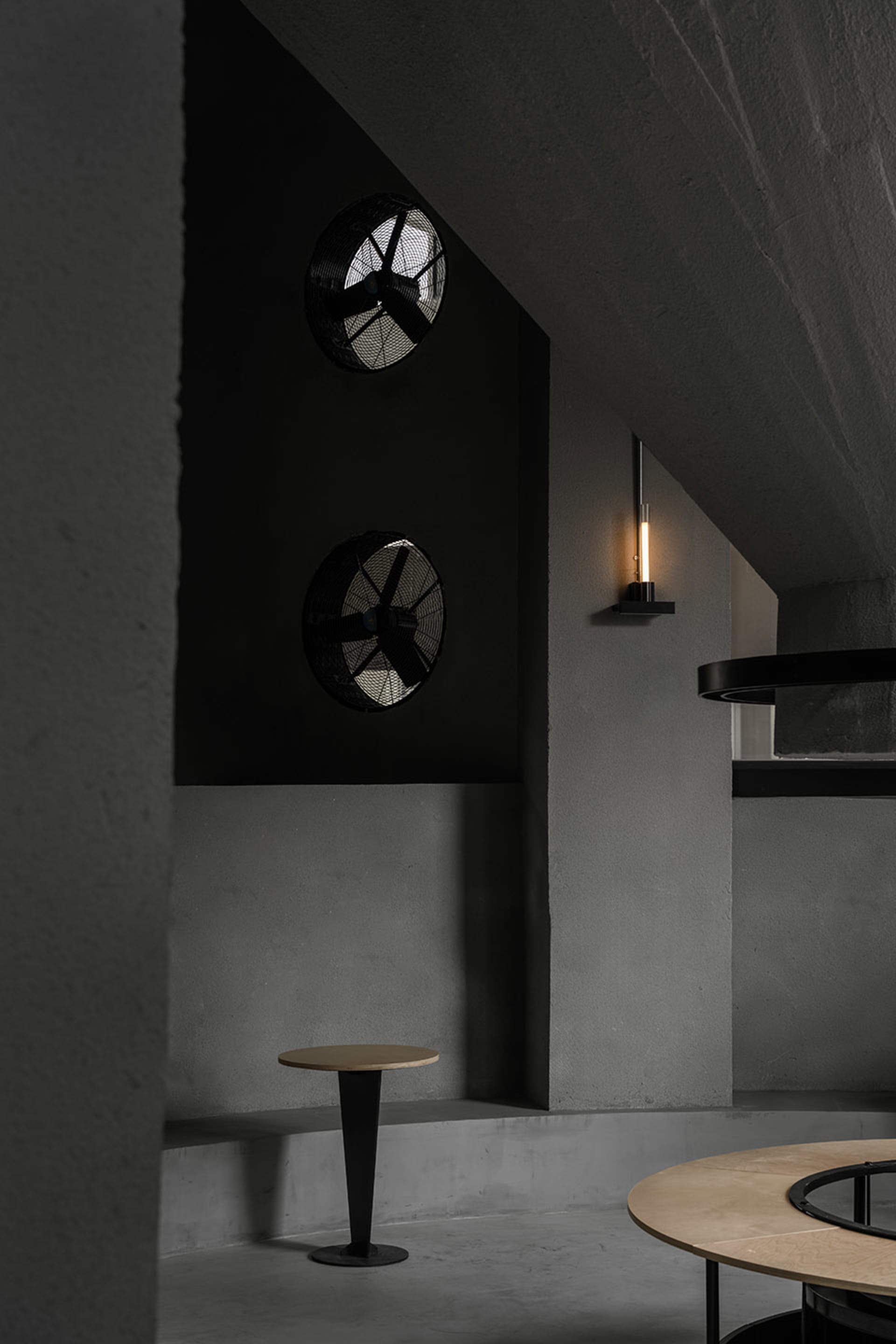 A modern interior design featuring a black wall with two clocks, one round and one square, and two lights, one above the clocks and one further down the wall