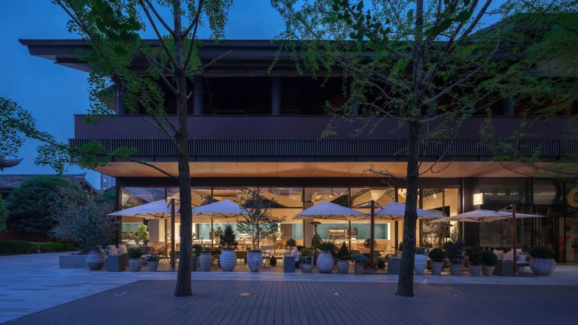Outdoor dining space with tables, chairs, umbrellas, and a mix of wood and metal materials under dim warm lighting