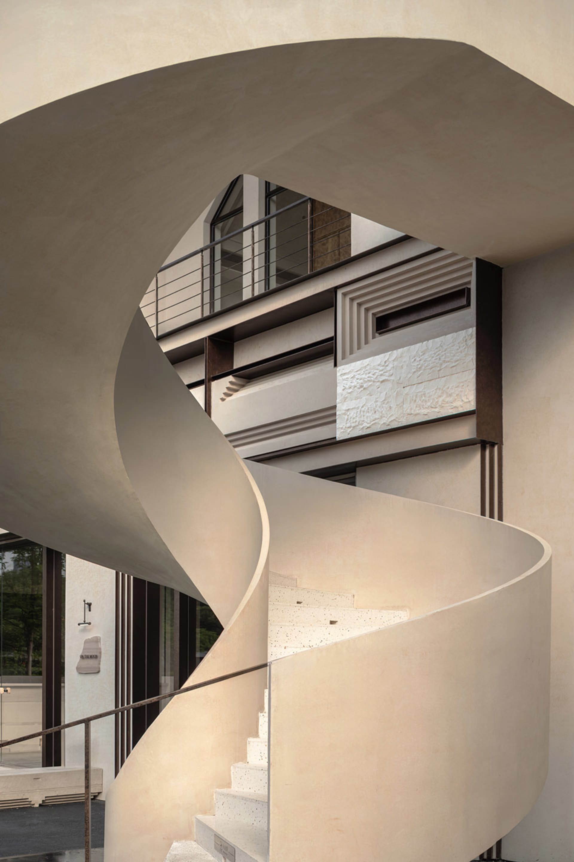 A modern building with a spiral staircase leading to another level, featuring large windows that allow natural light to enter the space, creating an atmosphere of elegance and sophistication