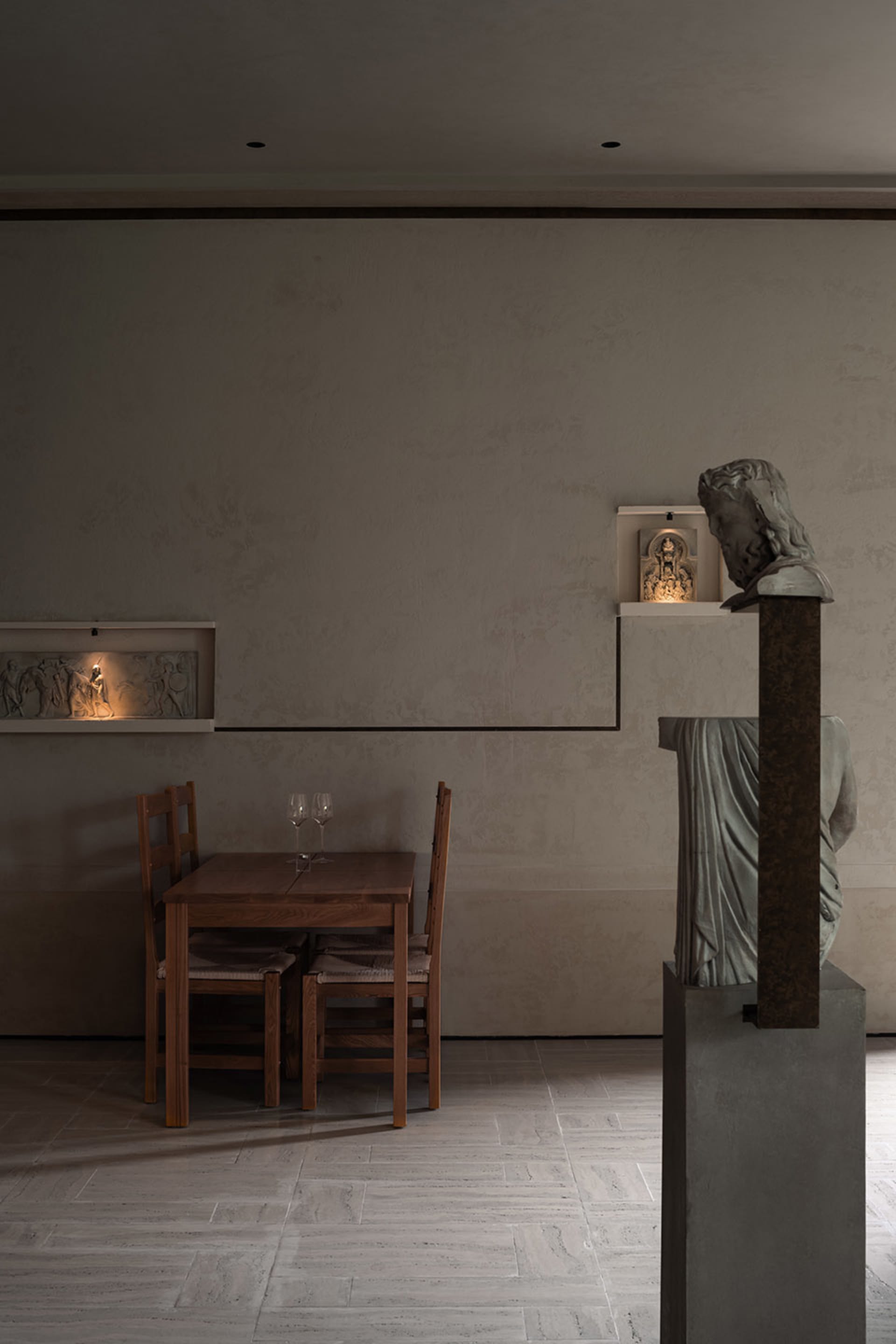 A calm and inviting dining area with a wooden table, chairs, wine glasses, and a cup, surrounded by a stone wall