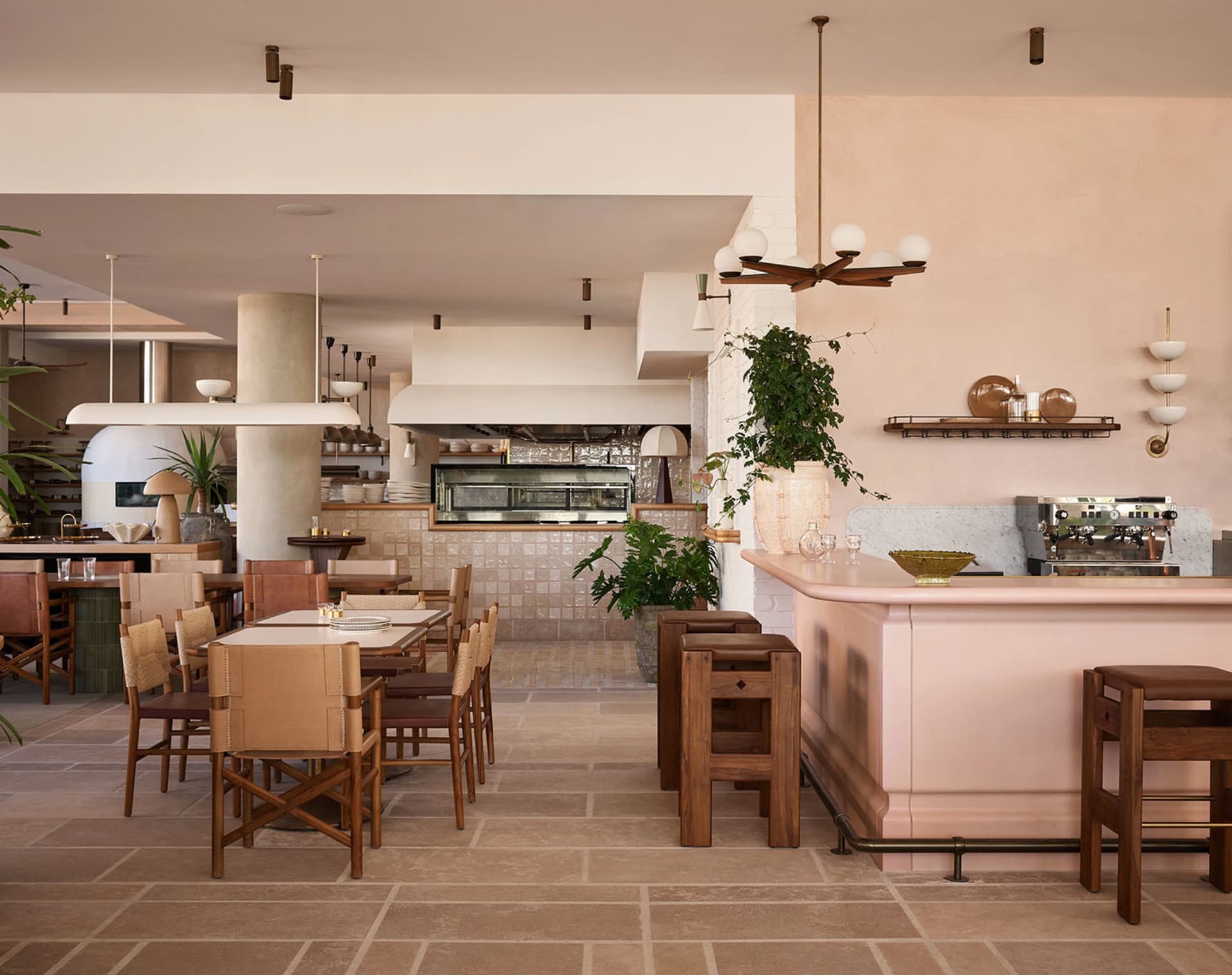 A modern restaurant with a pink bar, wooden furniture, and stone elements, featuring warm white and brown tones and overhead lighting