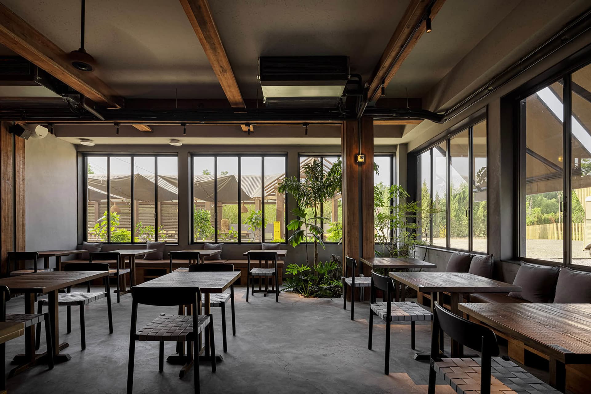 A restaurant interior with multiple round tables and chairs, some with cushions, arranged for socializing and dining