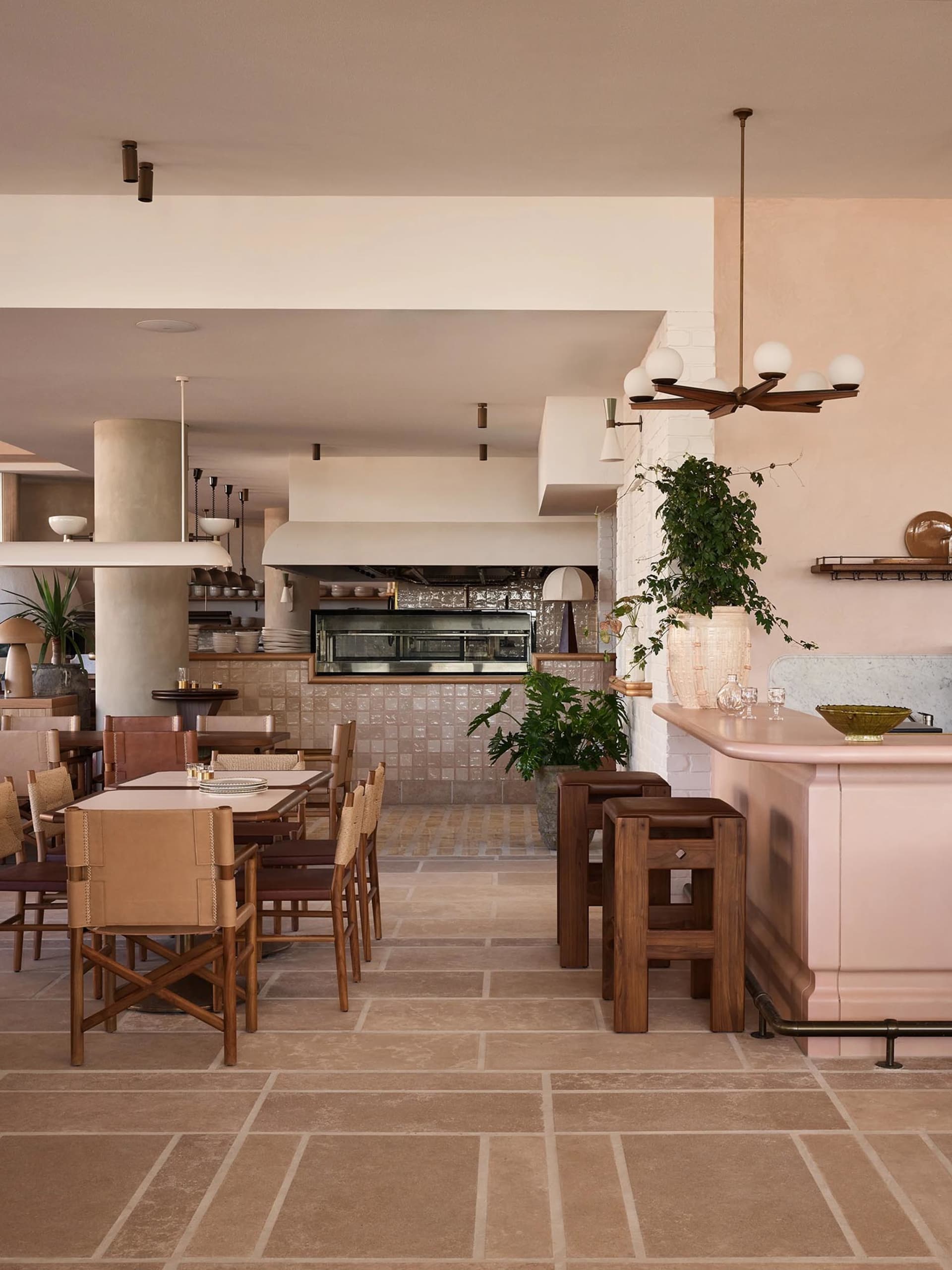 Modern restaurant interior with pink walls, white ceiling, and potted plants, featuring a spacious dining area with tables and chairs