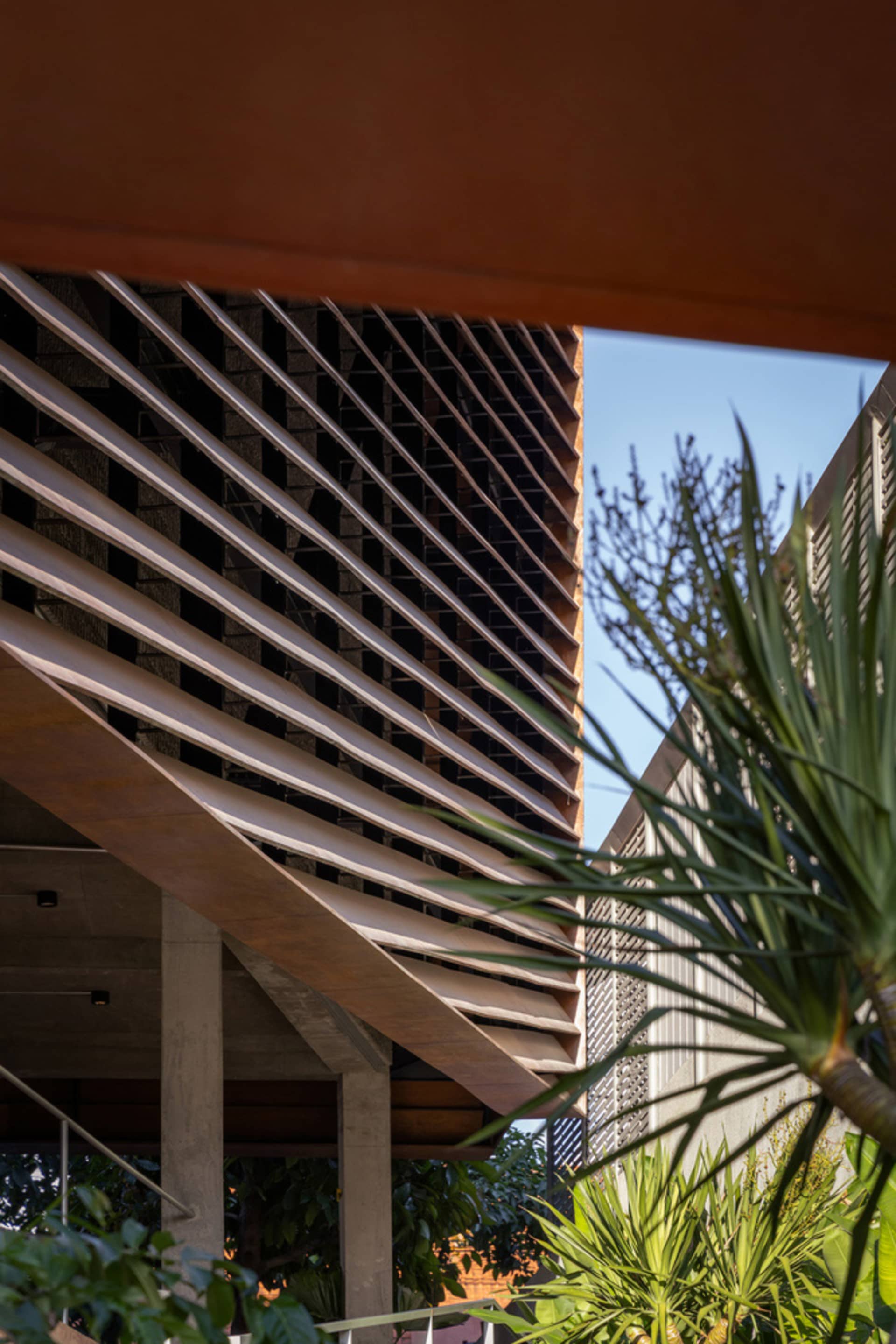 A modern high-rise building with a concrete exterior and large windows, set against a backdrop of palm trees in an urban environment