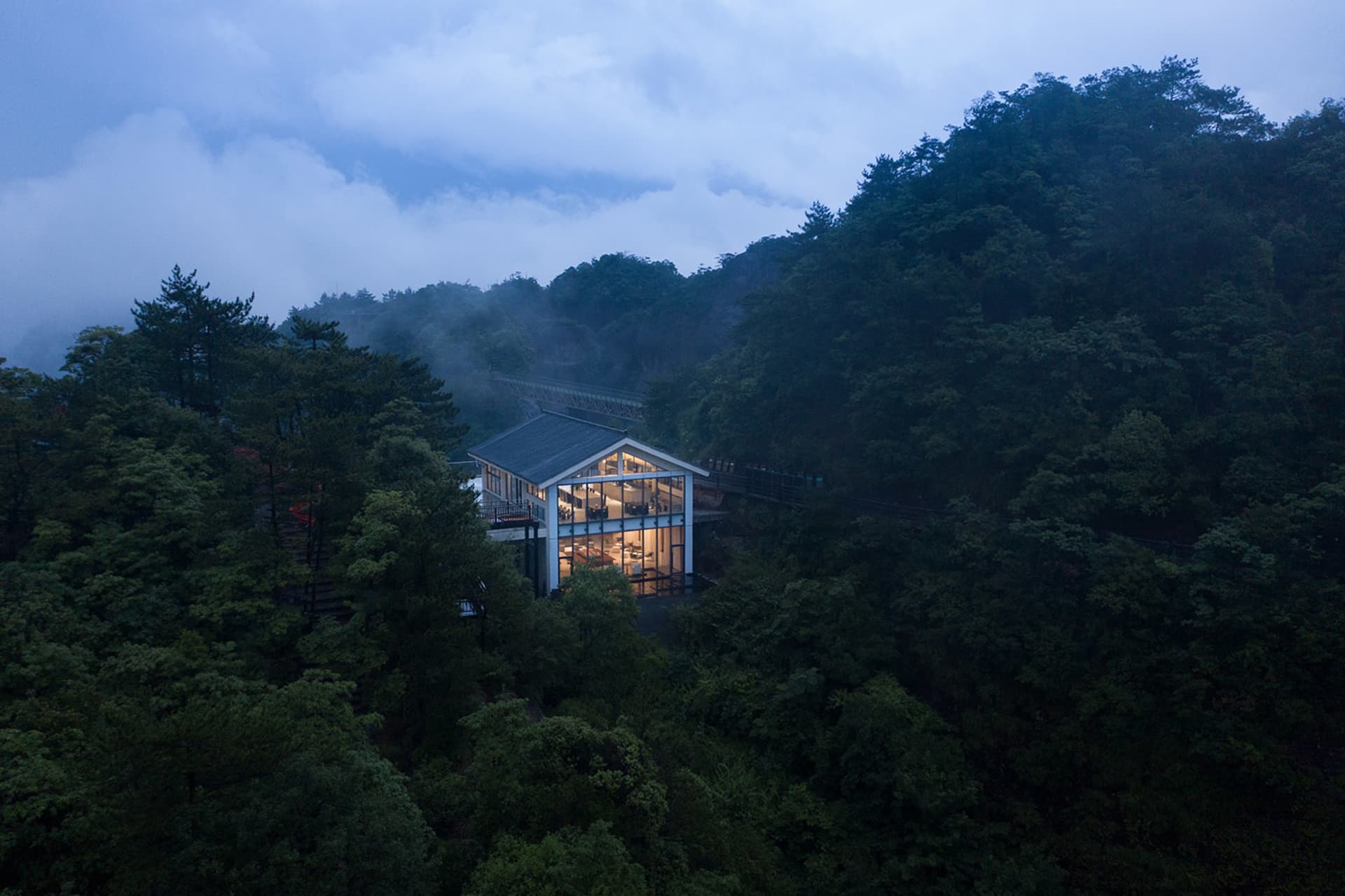 A modern building with large windows, situated in a serene forest environment with surrounding trees