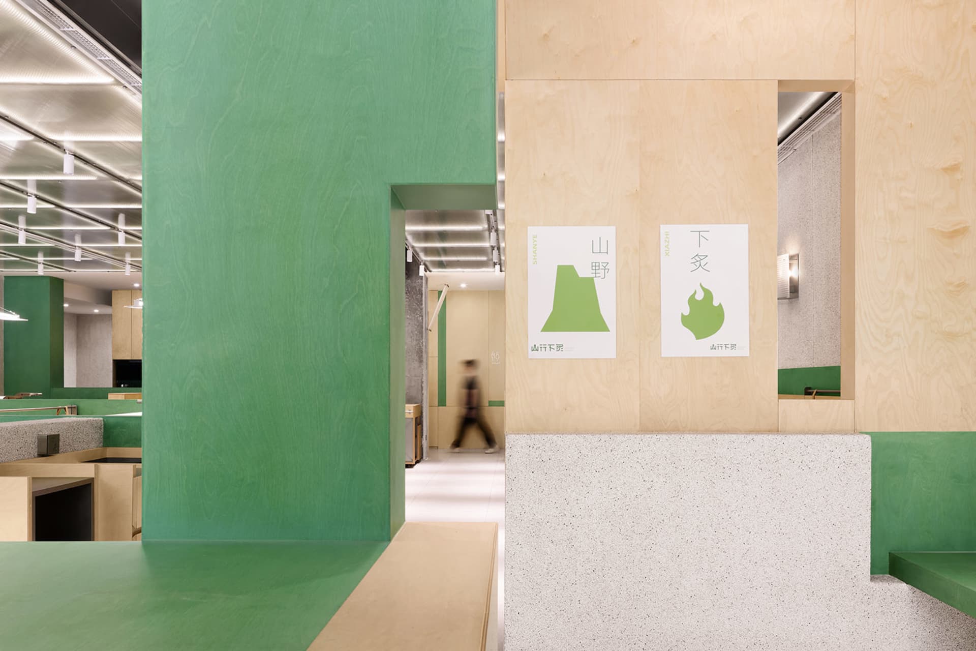A calm and orderly hallway with a green wall, wooden panels, and a white floor, featuring two people walking down the hallway