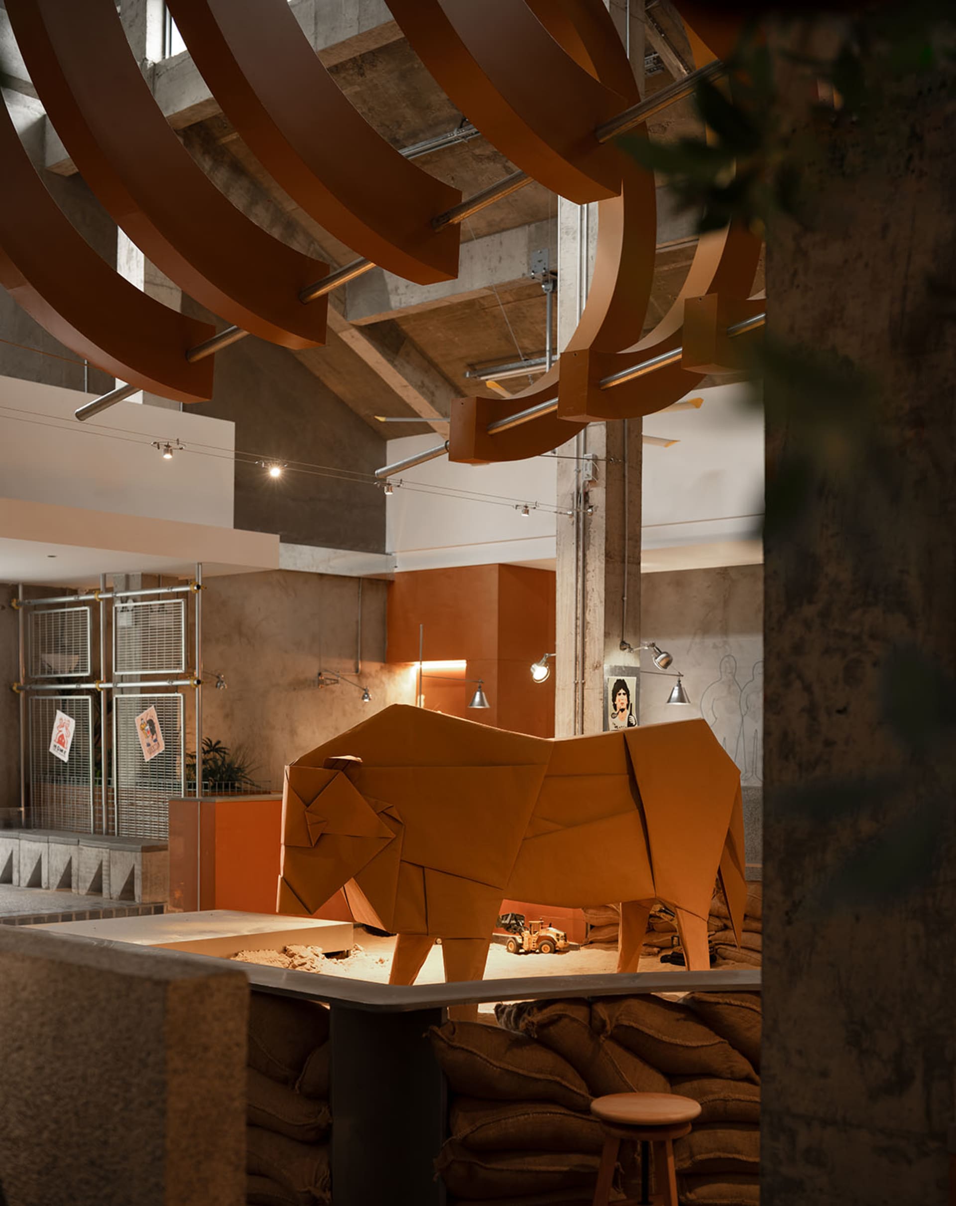 A creative living space with a cardboard bull sculpture, potted plants, and a chair, set against a neutral background