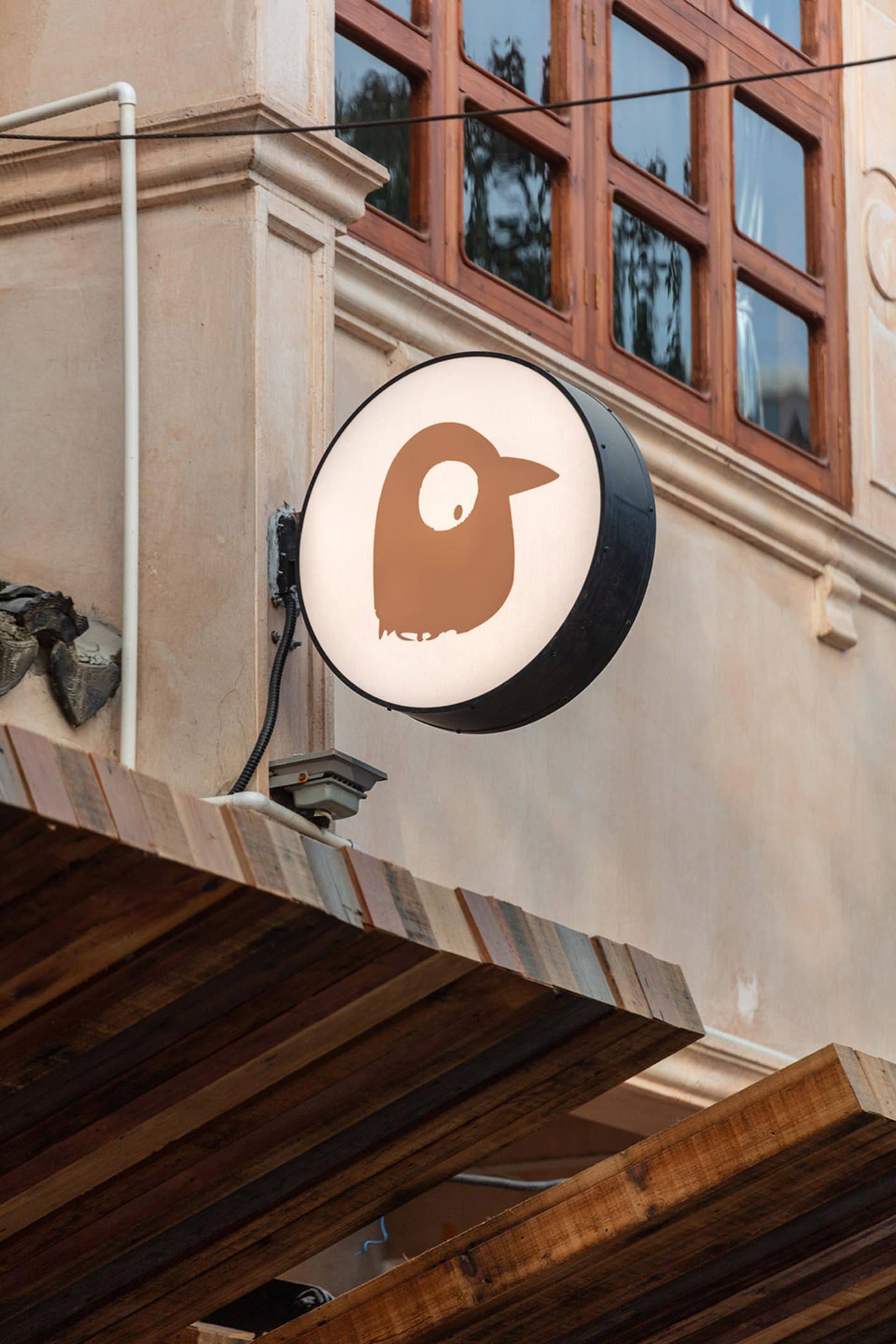 Modern building exterior with a lit bird logo on the facade, white walls, and two clocks on the wall