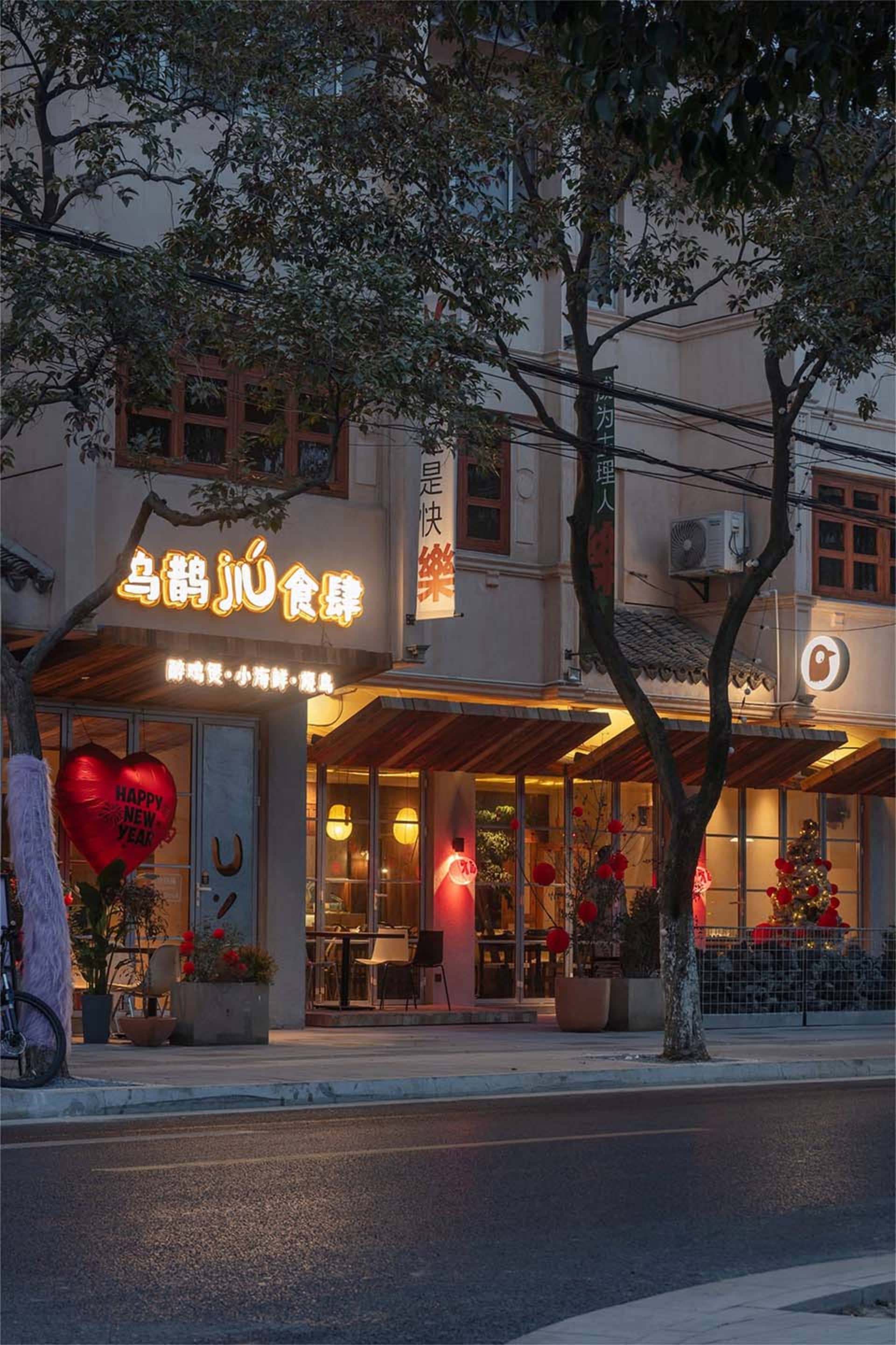 A white building with red accents and outdoor seating area with potted plants, creating a warm and inviting atmosphere at night