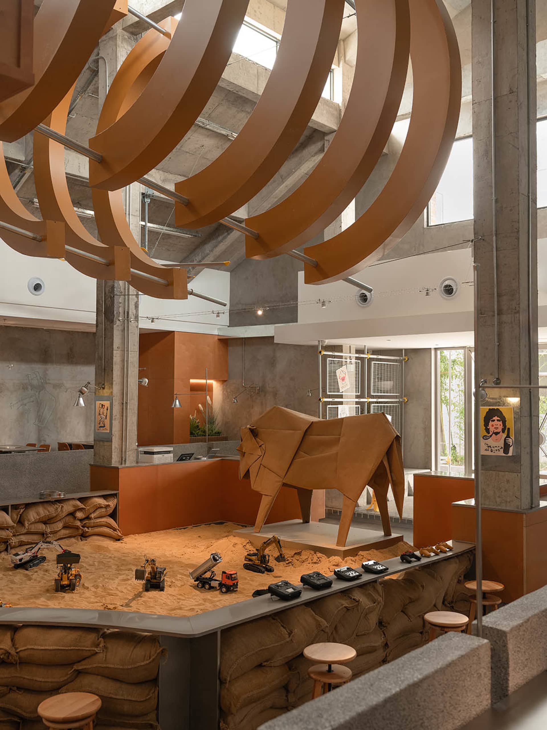 A room with a sandy floor, a large wooden elephant sculpture, and several chairs and potted plants, creating a unique and creative atmosphere