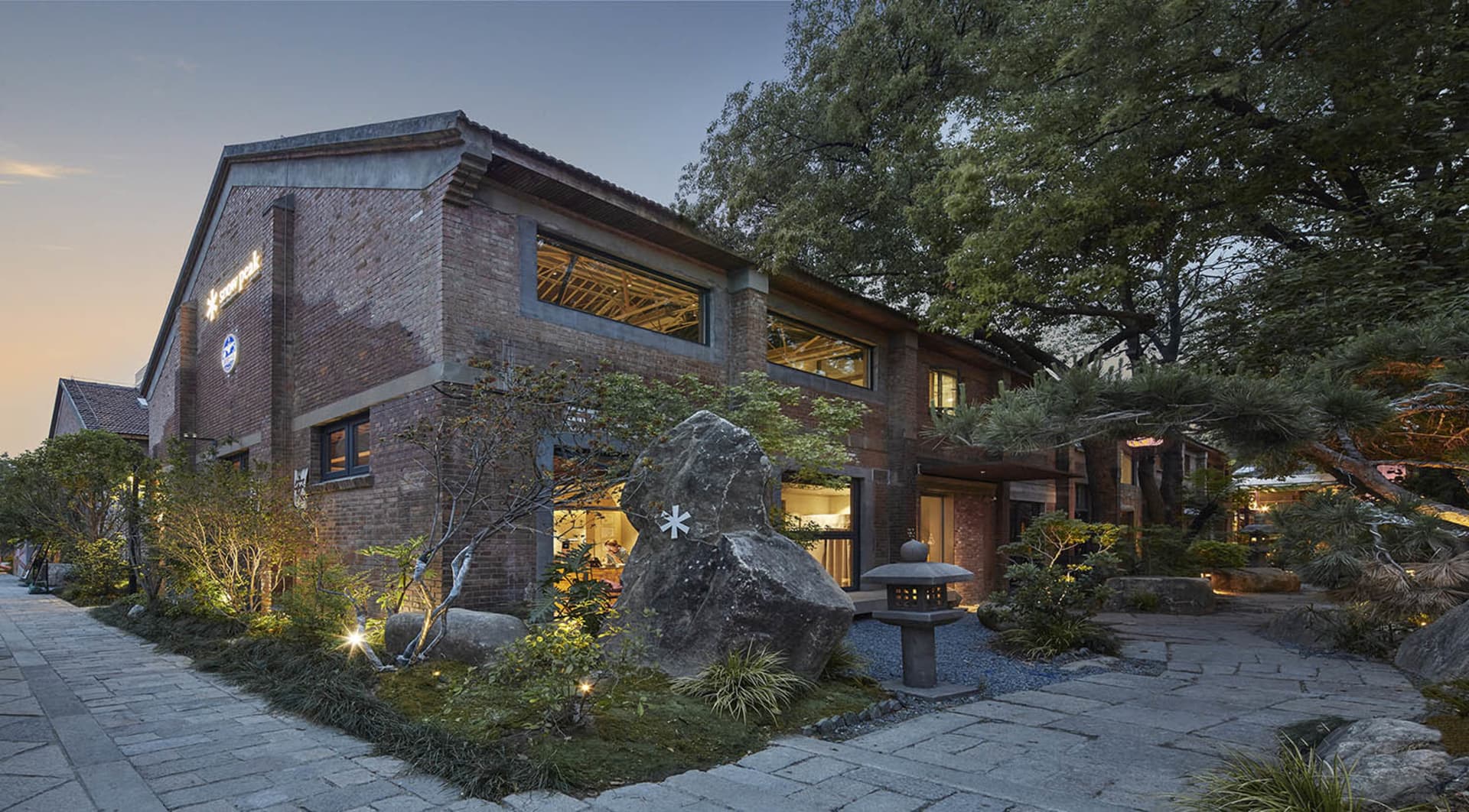 Asian-style building with a brick facade, featuring a large rock in front of it, and several windows on its exterior