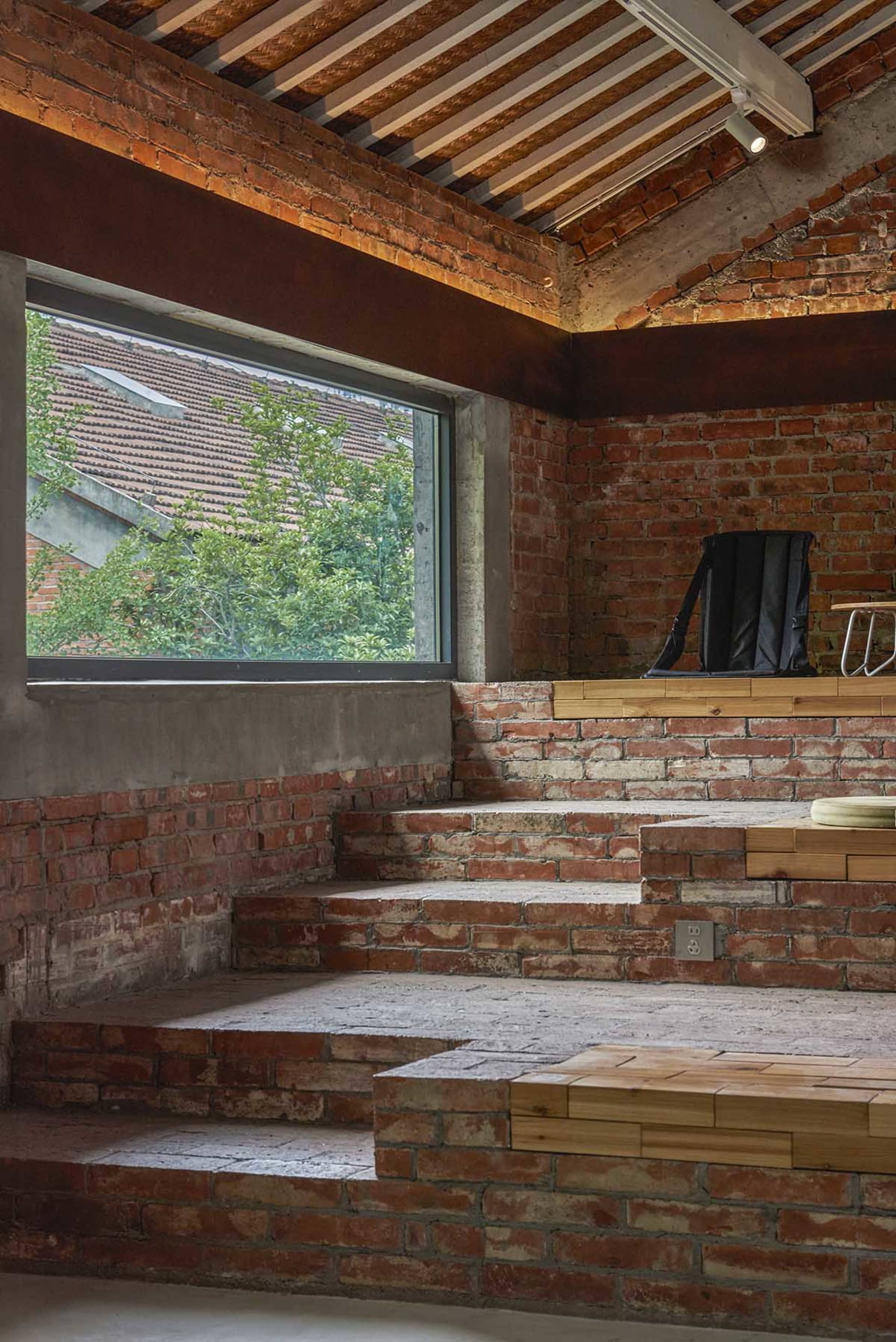 Interior of a brick building with a large window, two chairs, and a dining table, bathed in natural light