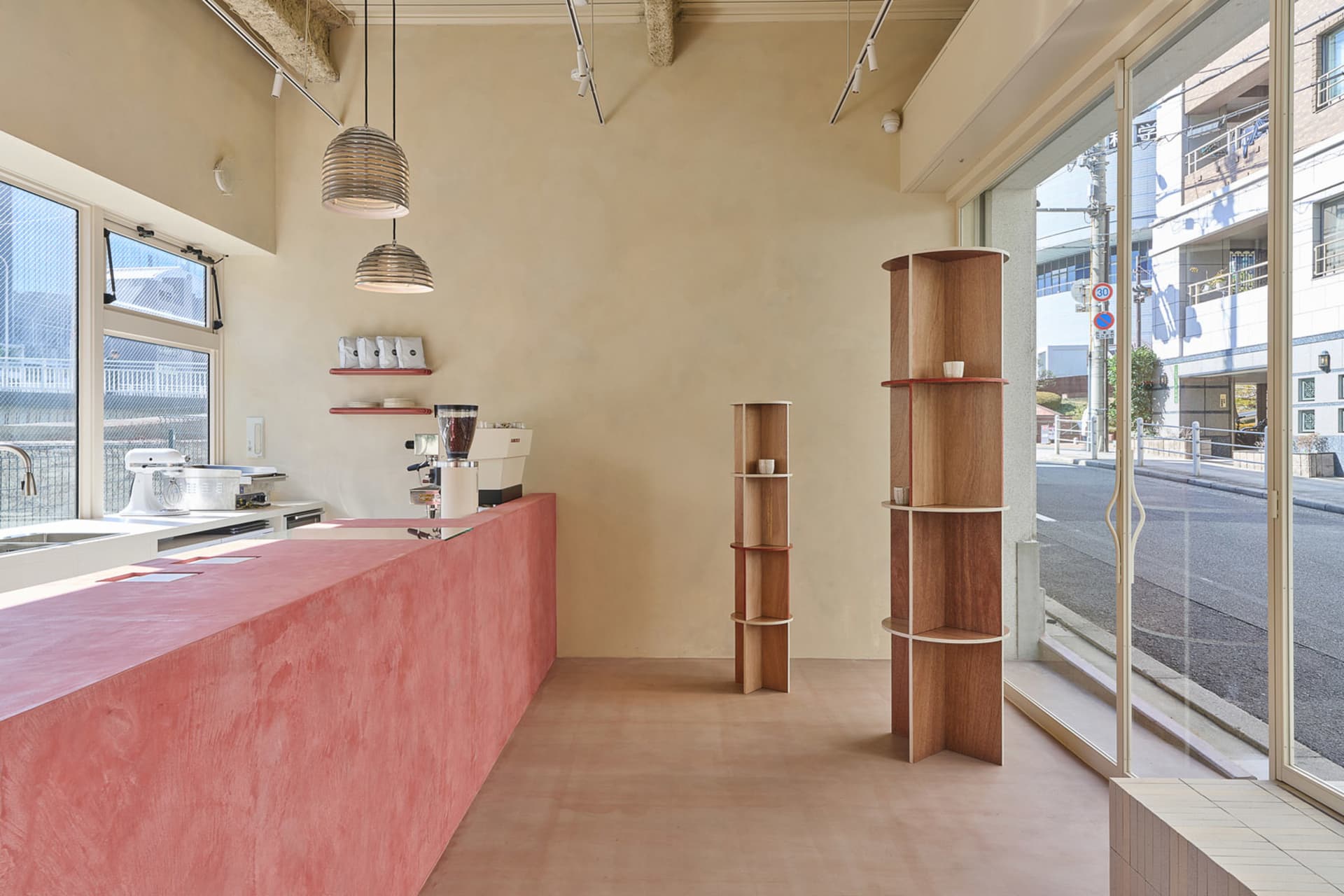 Cozy cafe interior with a pink countertop, wooden shelves, and beige walls, featuring books, cups, and other items
