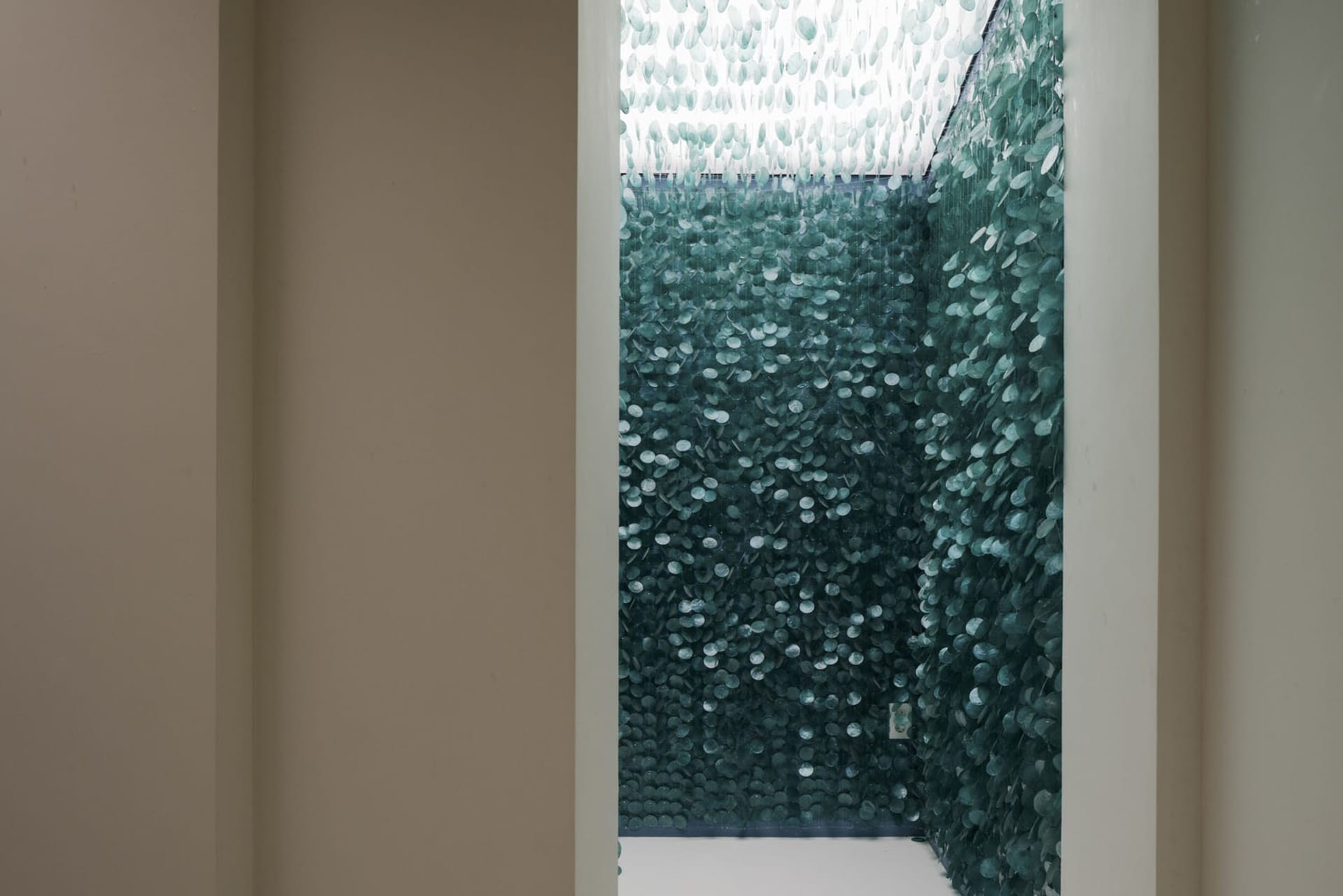 Modern bathroom with a large glass wall featuring green glass pieces and small windows, allowing natural light to enter the space