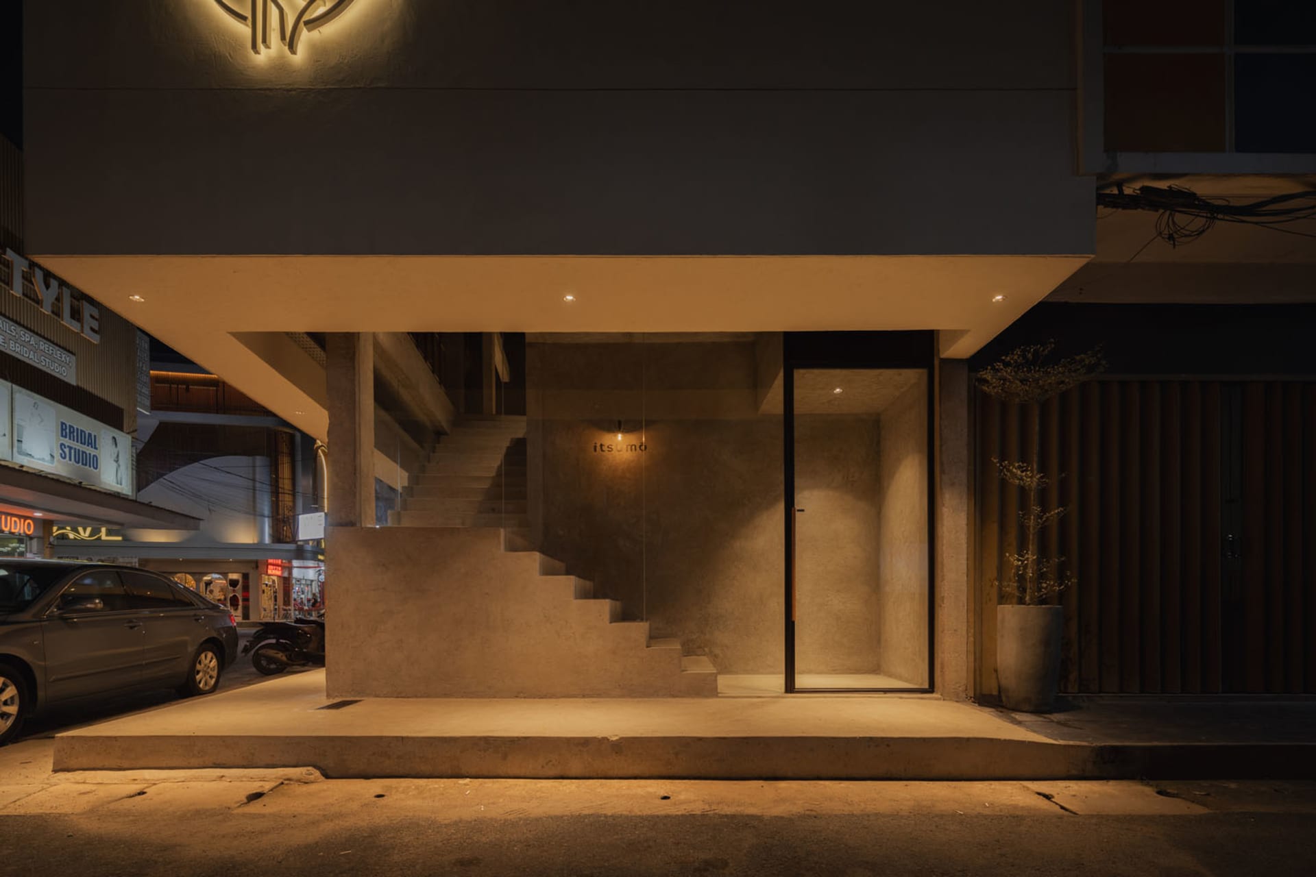 A modern building with a concrete staircase leading to a doorway, set against a dark background with a potted plant near the corner